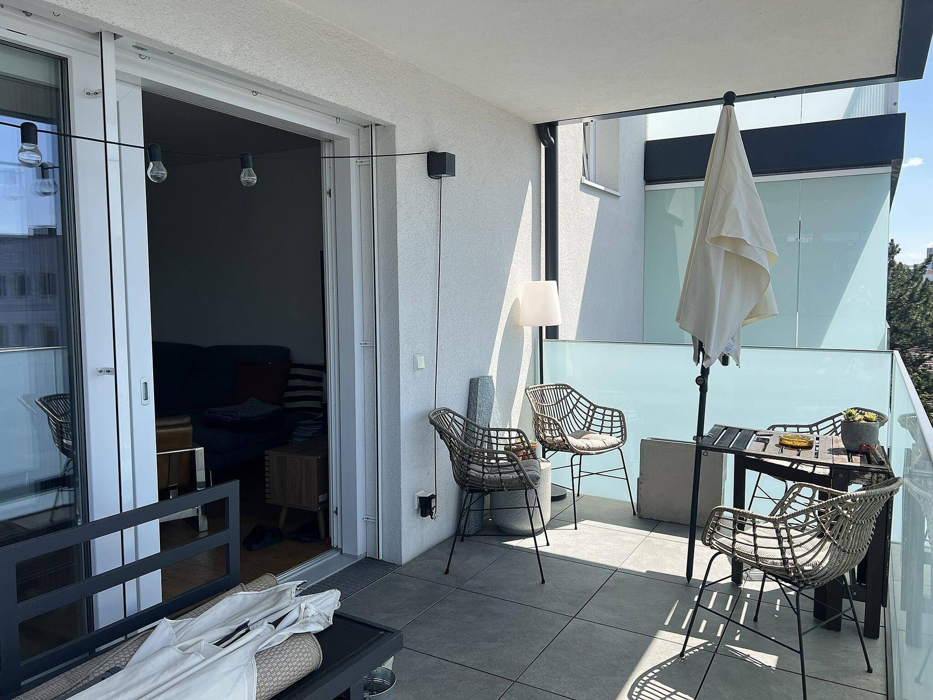 Großer Balkon mit Sitzmöbeln, Sonnenschirm und Zugang zum Innenbereich der Wohnung.
