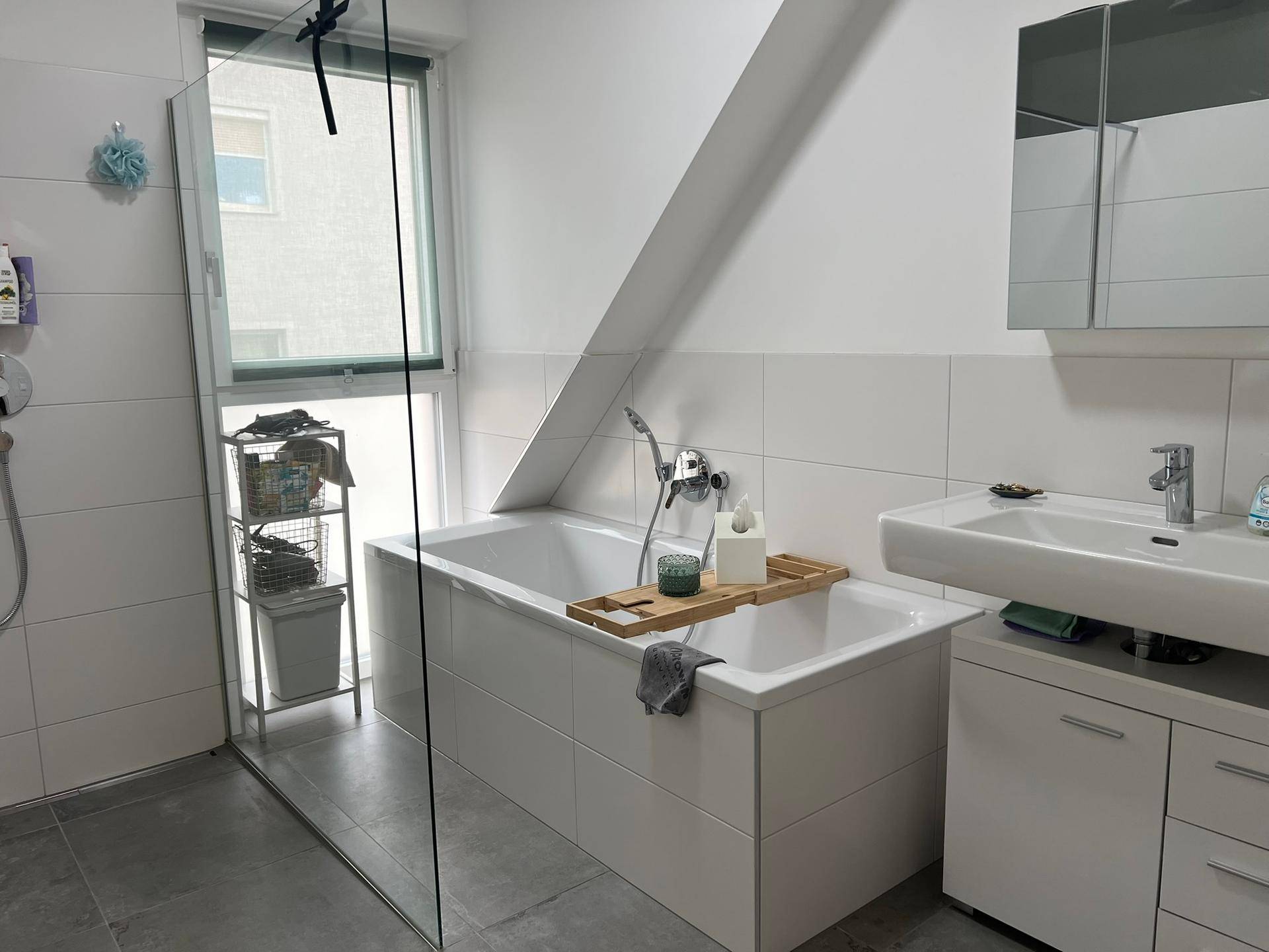 Modernes Badezimmer mit Badewanne, Duschbereich und Fenster, hell gefliest.