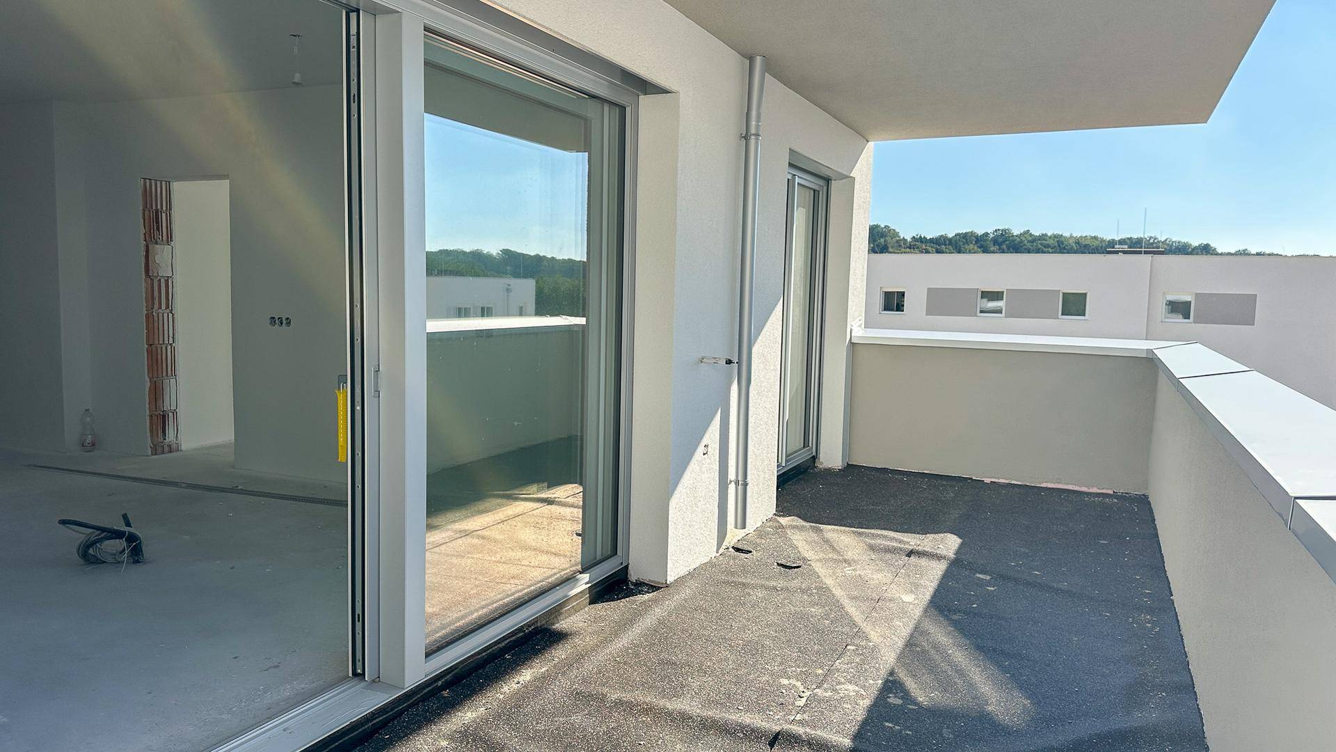 Unfertiger Balkon mit Schiebetüren und Blick auf andere Neubauten in der Umgebung.