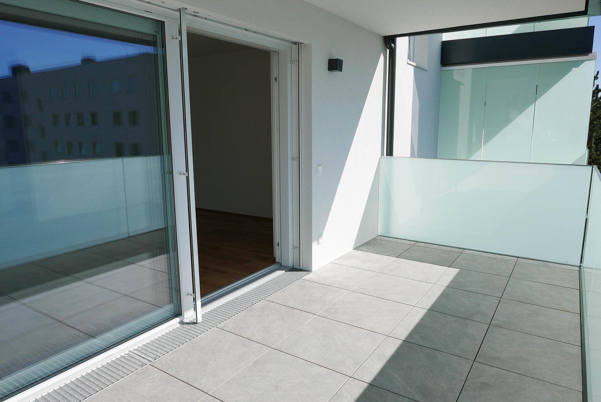 Neuer Balkon mit Fliesenboden und Glasbrüstung, zugänglich vom Wohnbereich.