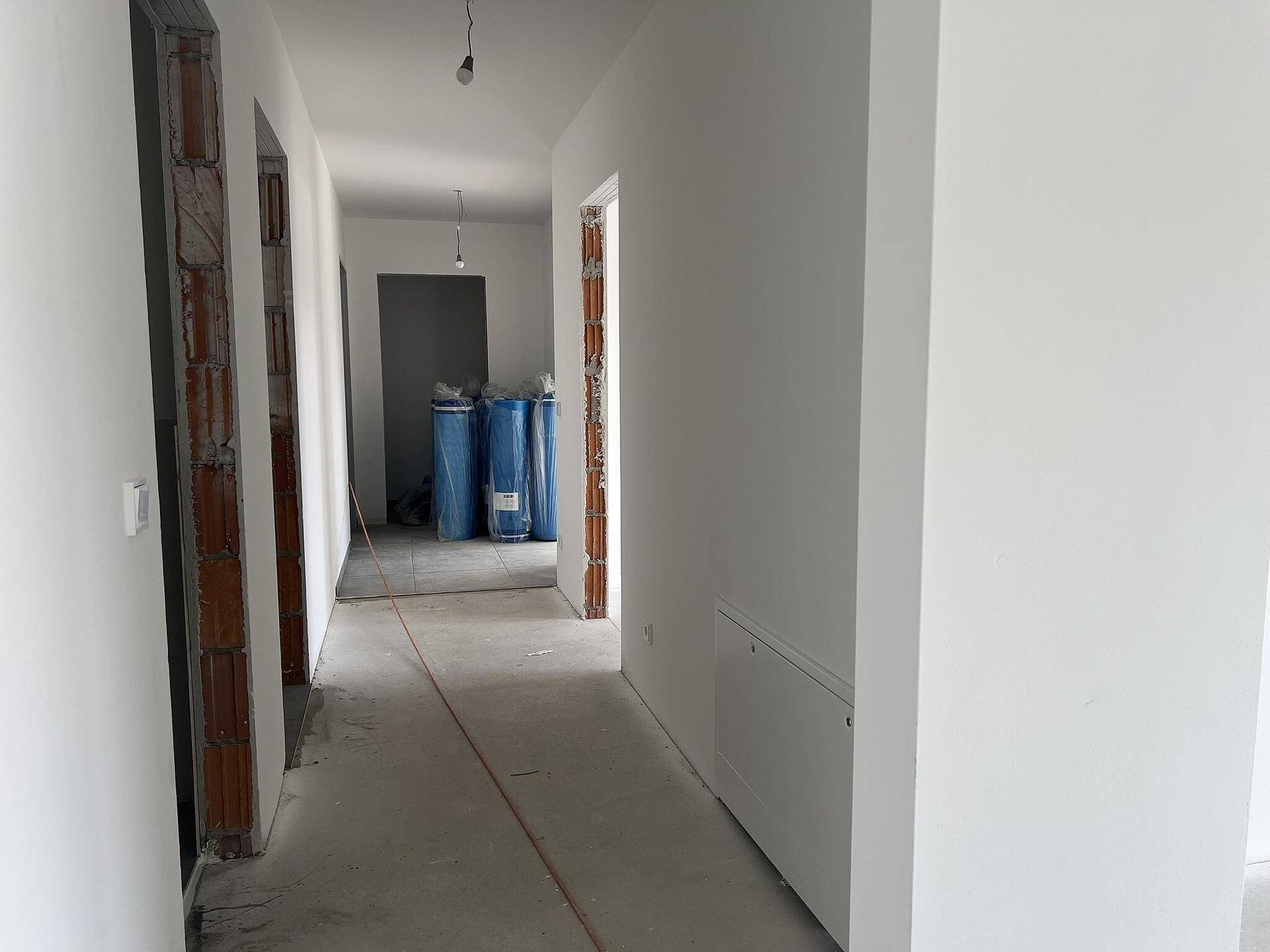 Langer, heller Flur in einem Neubau mit unverputzten Türrahmen und sichtbaren Baumaterialien.