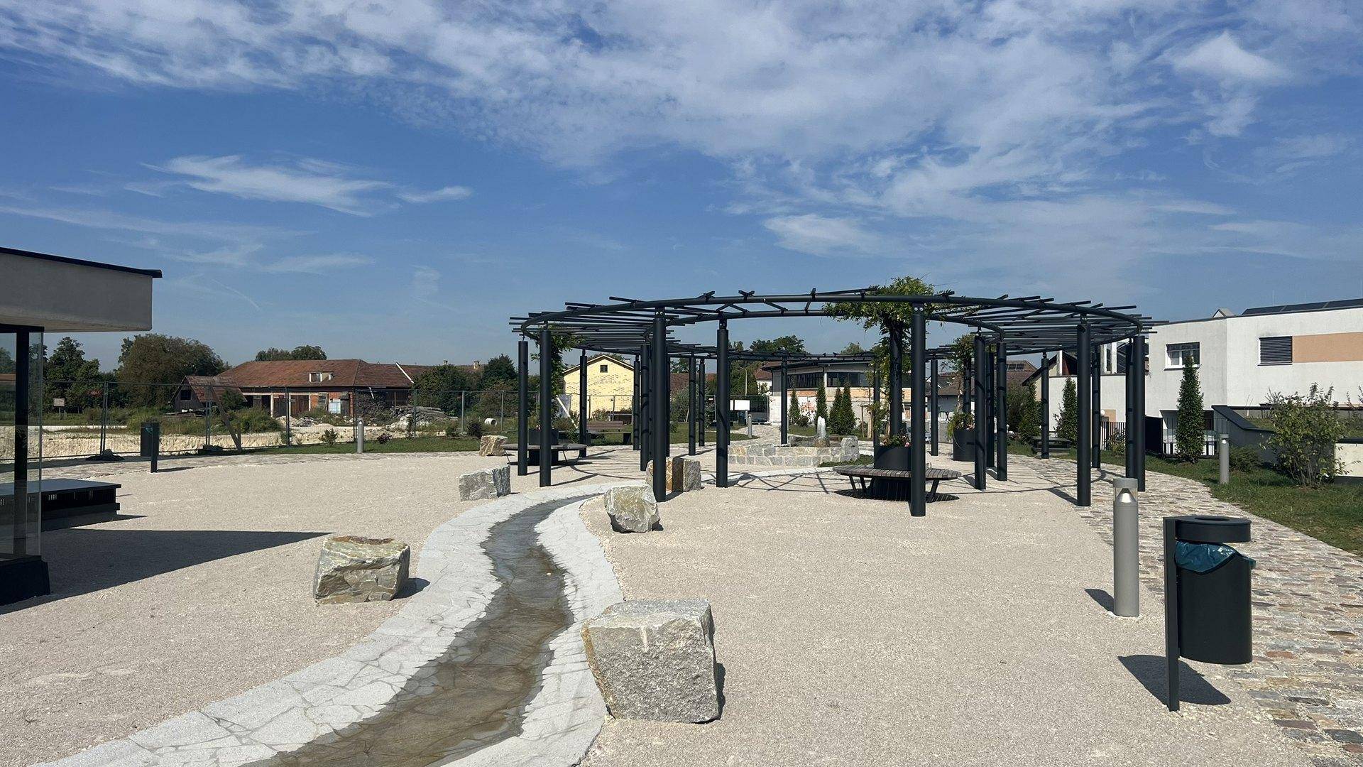 Ein weitläufiger Außenbereich mit Kieswegen, großen Steinen und einer modernen Pergola.