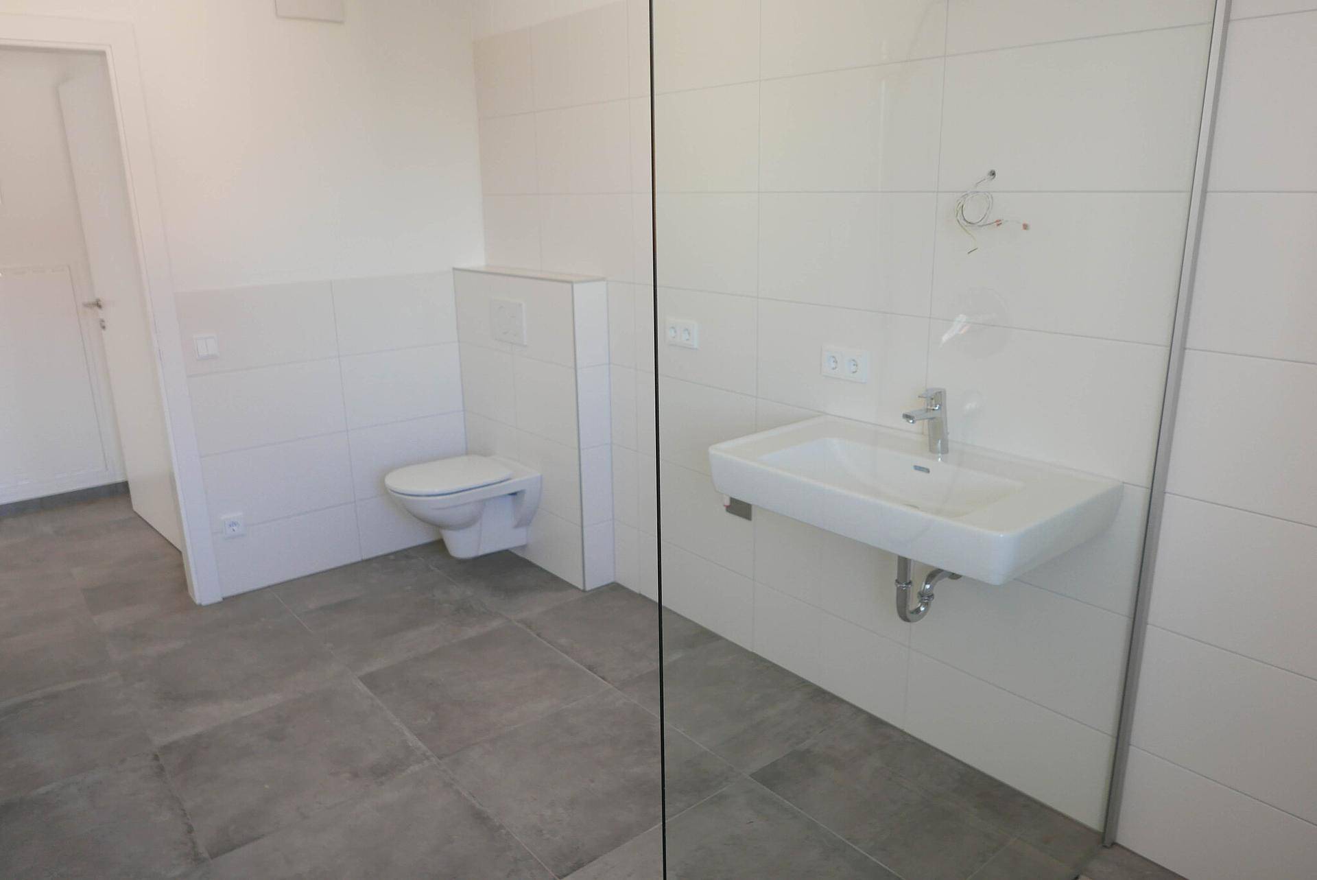 Modernes Badezimmer mit WC, Waschbecken und weißen Fliesen.