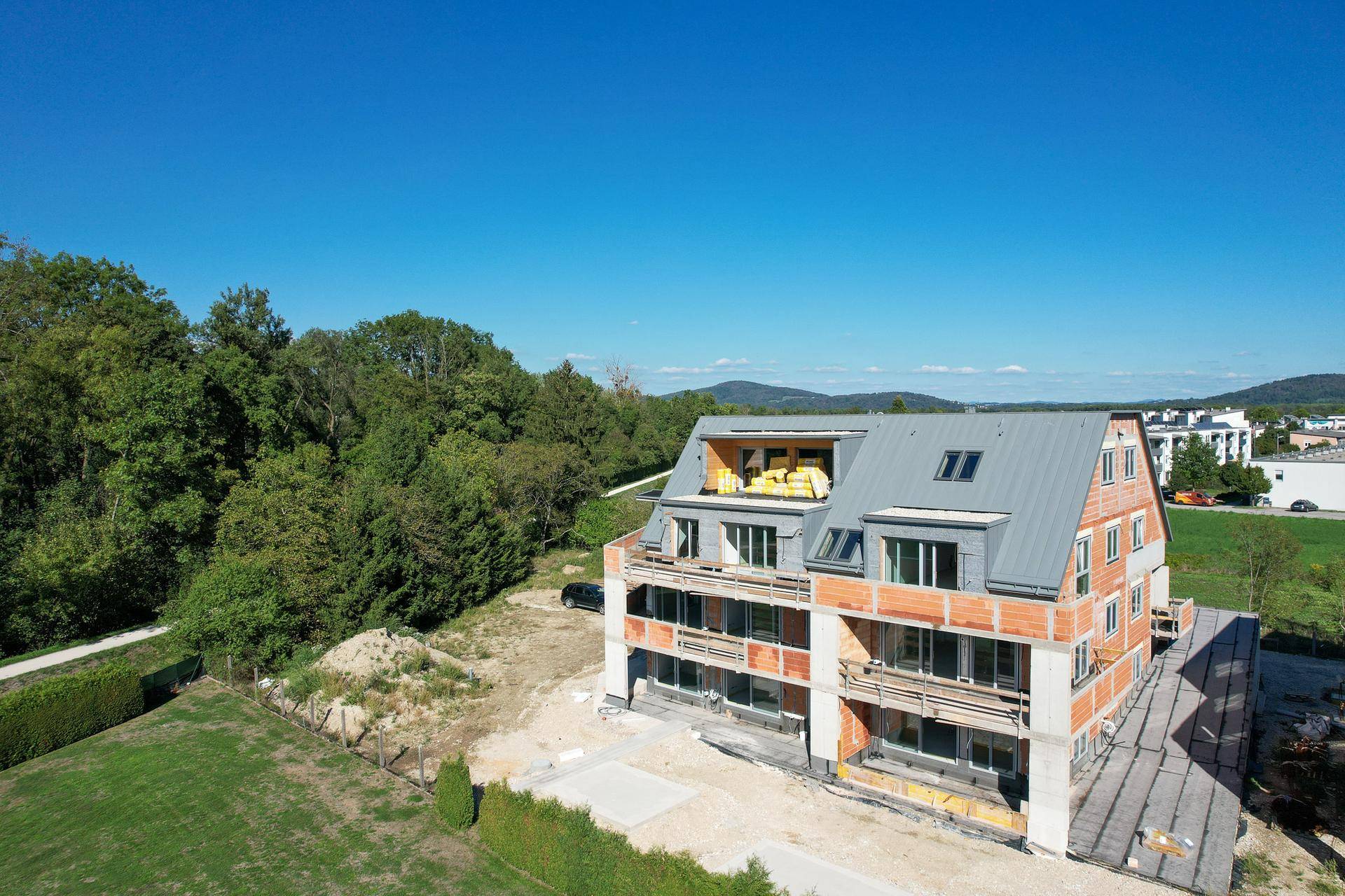 Neubau im Rohbau mit Blick auf bewaldete Hügel und die weite Landschaft unter klarem Himmel.