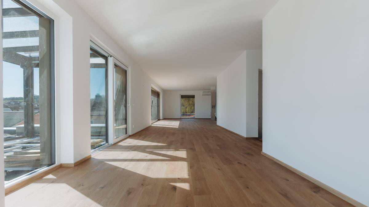 Heller, weitläufiger Raum mit Holzboden und bodentiefen Fenstern, die viel Tageslicht hereinlassen.