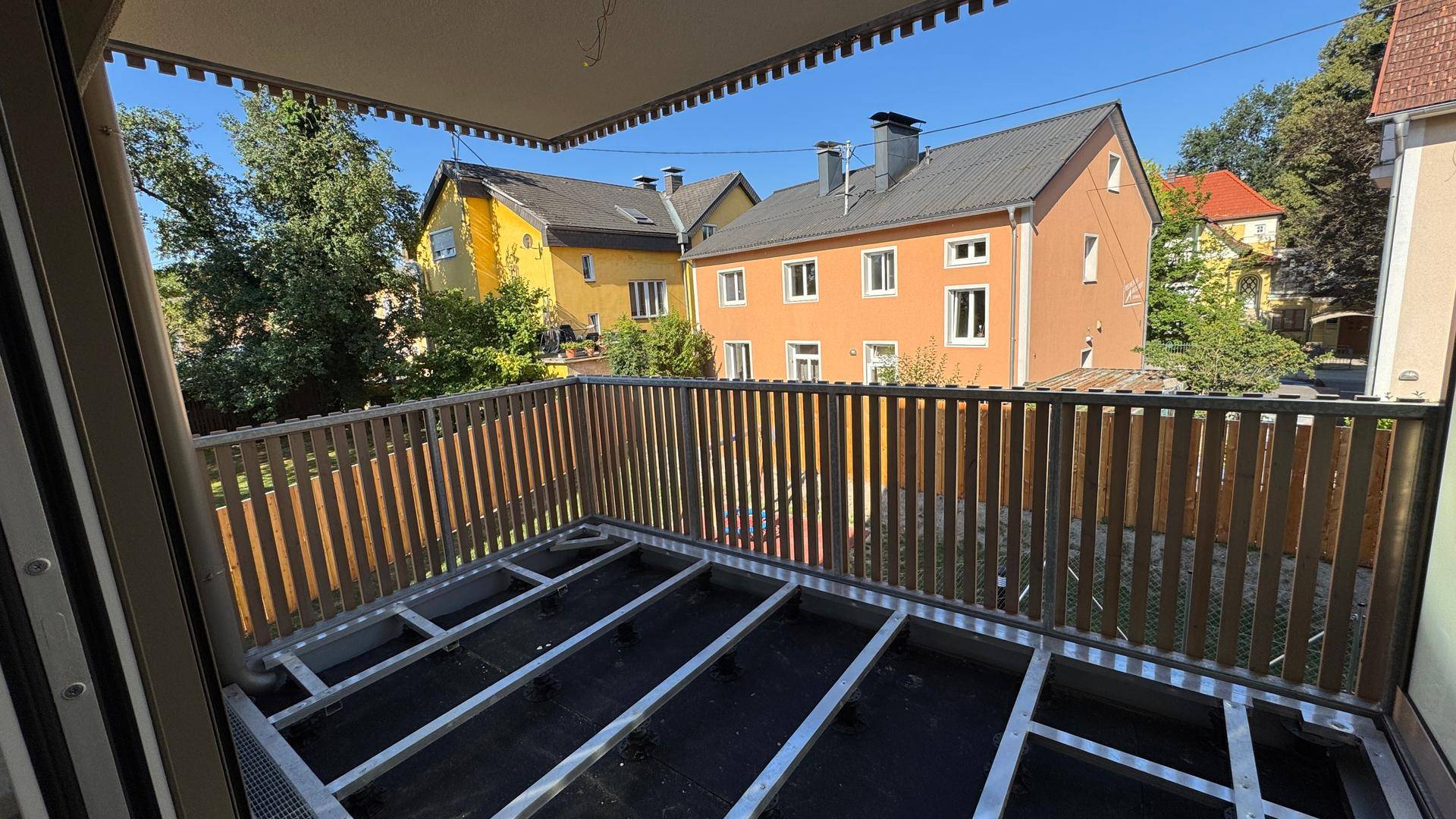 Balkon im Rohbau mit Holzgeländer und Metallunterkonstruktion, bietet Blick auf die Umgebung.