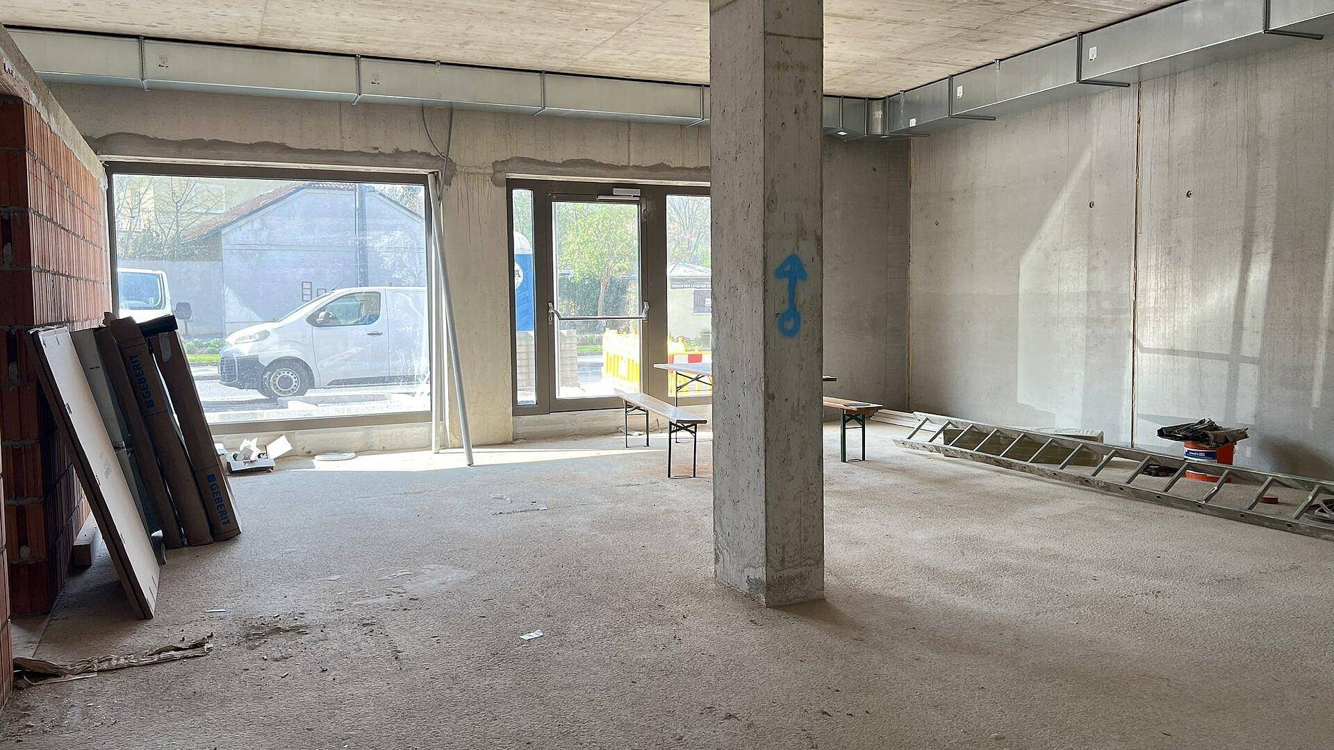 Offener Rohbau-Bereich mit Betonstütze und großen Fenstern, die den Raum mit natürlichem Licht füllen.