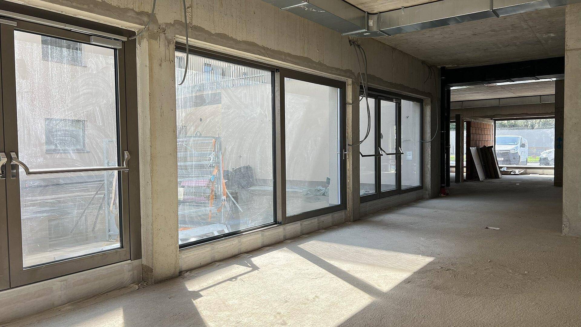 Heller Rohbau-Innenraum mit großen Fensterfronten und einer Glastür, die viel Tageslicht hereinlassen.