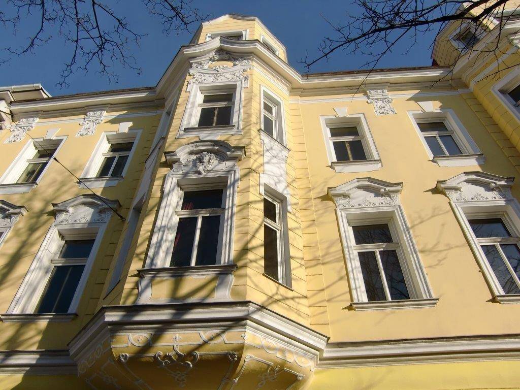 Historische Fassade eines gelben Gebäudes mit kunstvollen Stuckverzierungen und Erkerfenstern.
