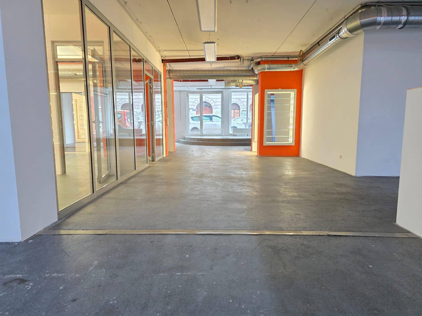 Langer, offener Gewerberaum mit Glaswänden zu angrenzenden Bereichen und Blick auf die Straße durch die Fenster.