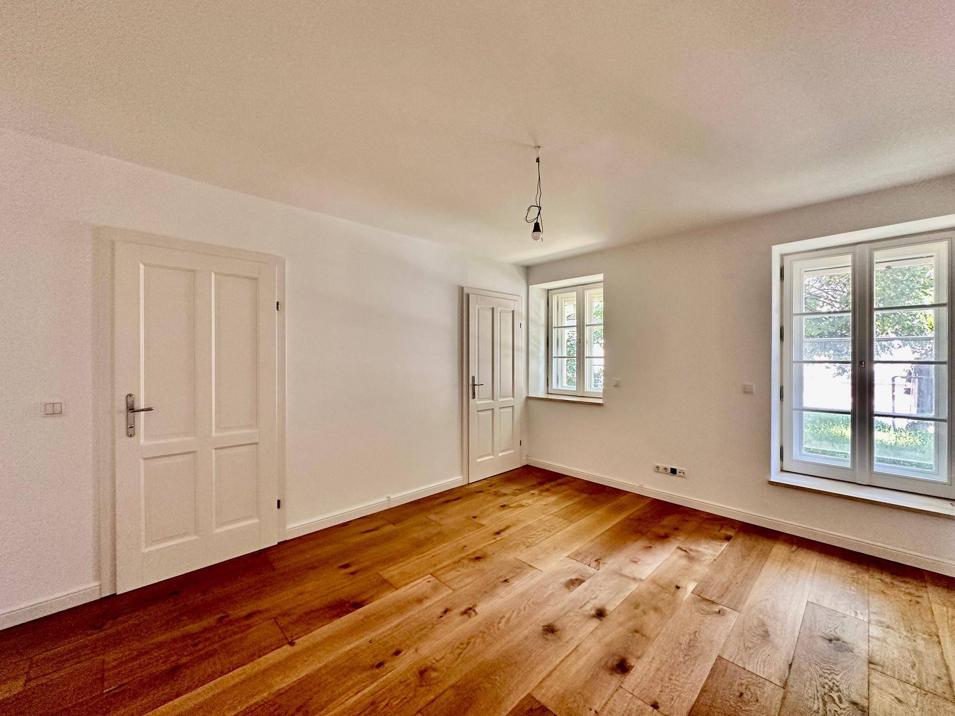 Helles Schlafzimmer mit Holzboden und zwei Fenstern, bereit zur individuellen Gestaltung.