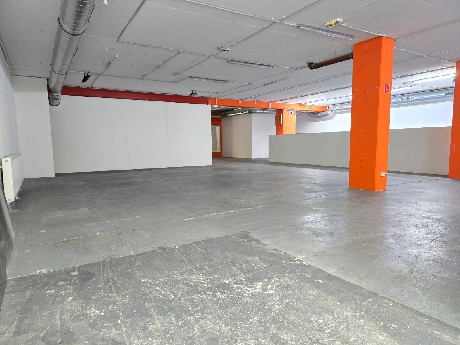 Weitläufiger Gewerberaum mit orangefarbenen Trägern und Säulen, sowie sichtbaren Lüftungsleitungen an der Decke.
