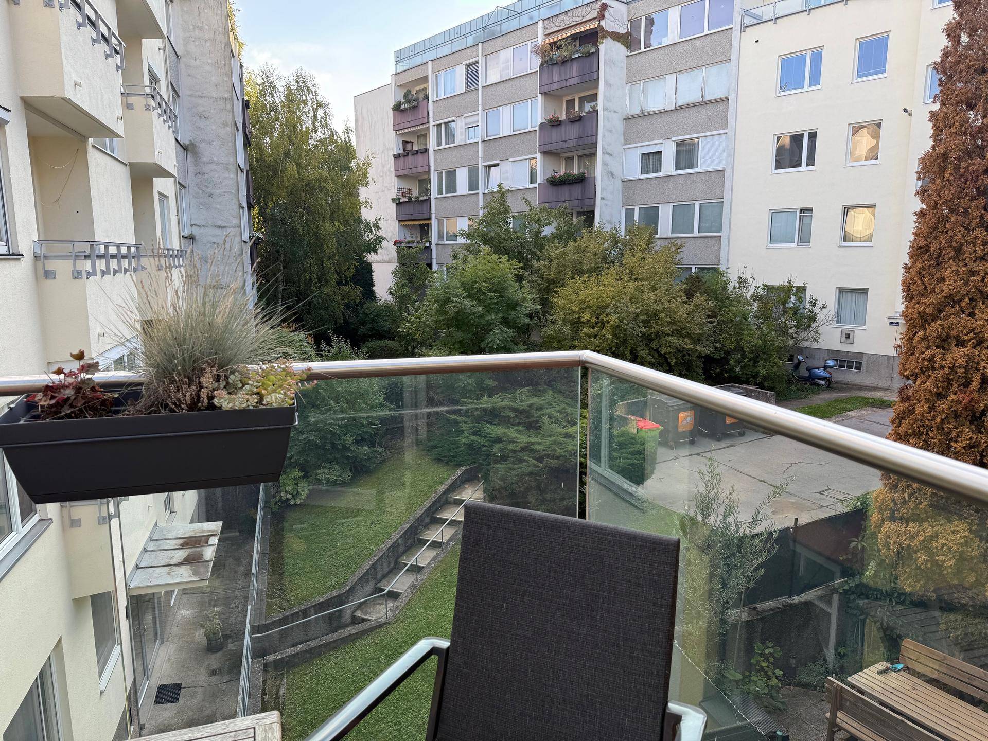 Balkon mit Sitzgelegenheit und Blick auf den begrünten Innenhof zwischen den Gebäuden.