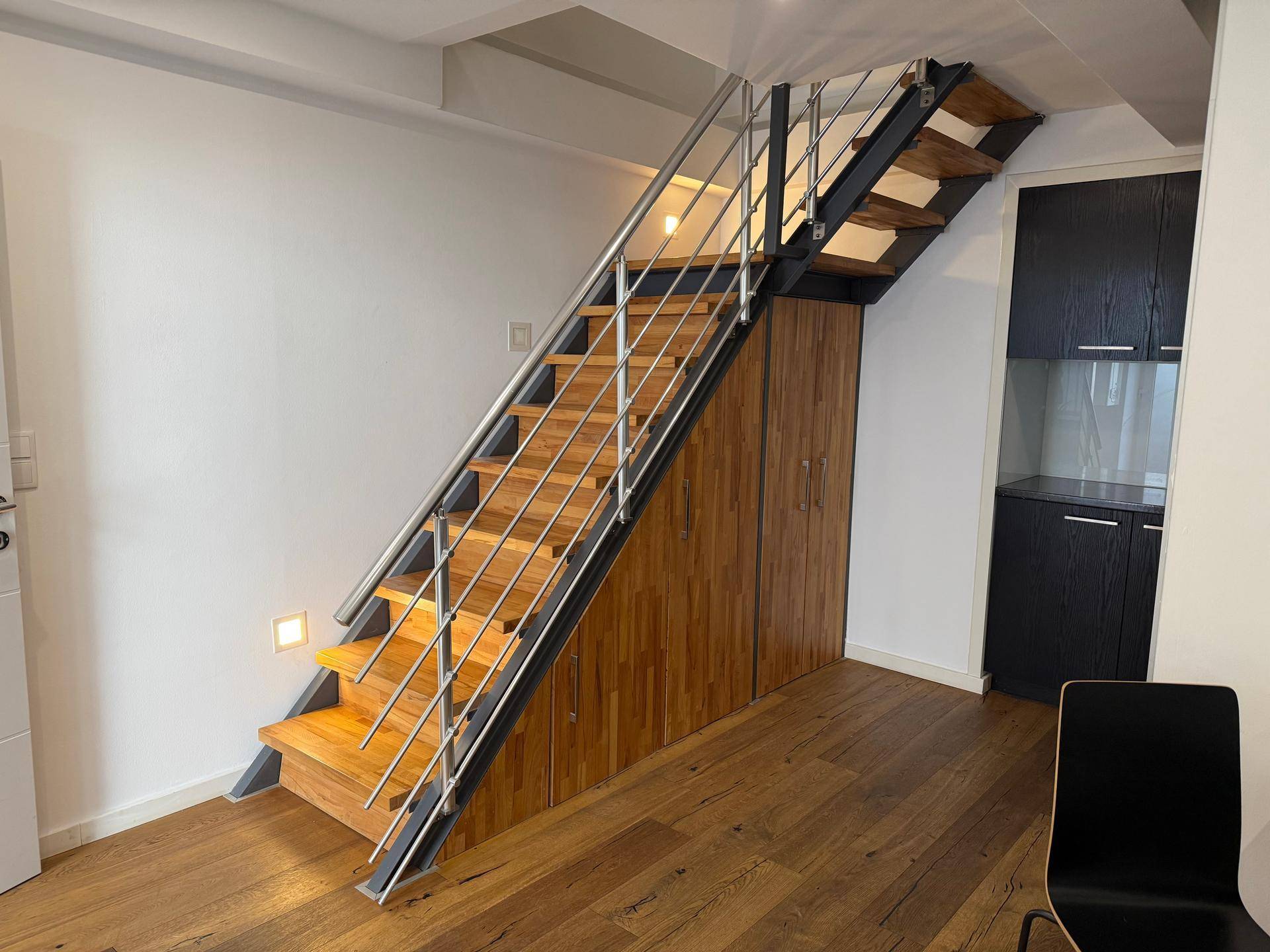 Moderne Holztreppe mit Edelstahlgeländer und integrierten Holzschränken im Flurbereich.