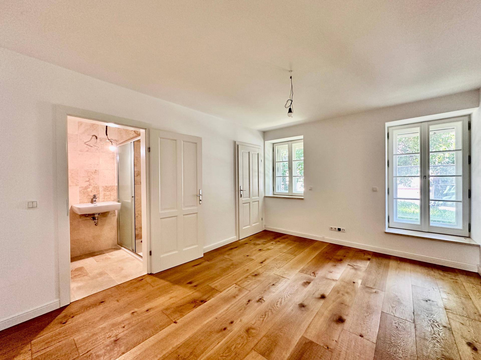 Schlafzimmer mit Holzboden und Zugang zu einem modernen Badezimmer mit Fliesen.