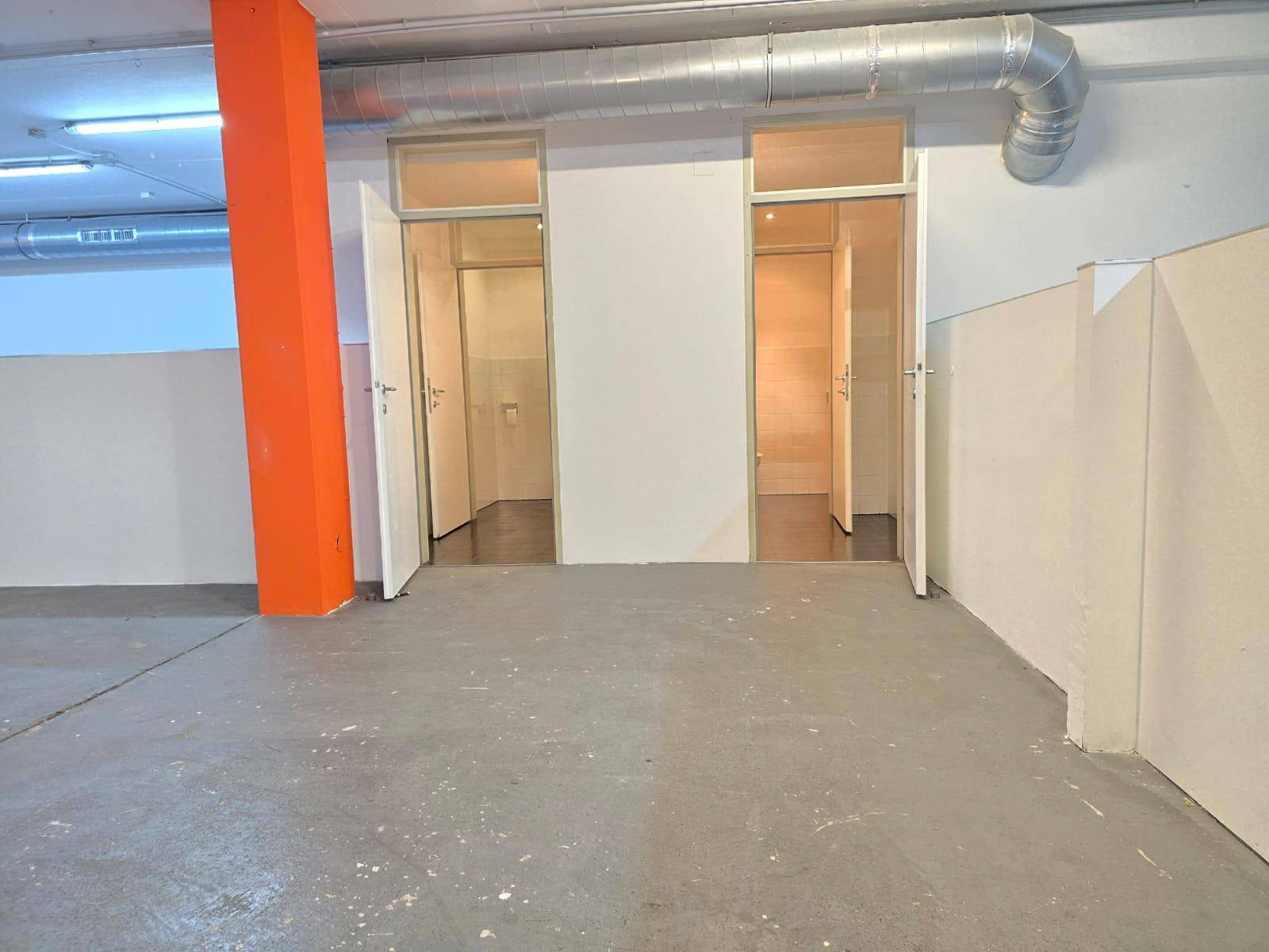 Gewerbefläche mit Betonboden, orangefarbenem Pfeiler und zwei offenen Türen zu Nebenräumen.