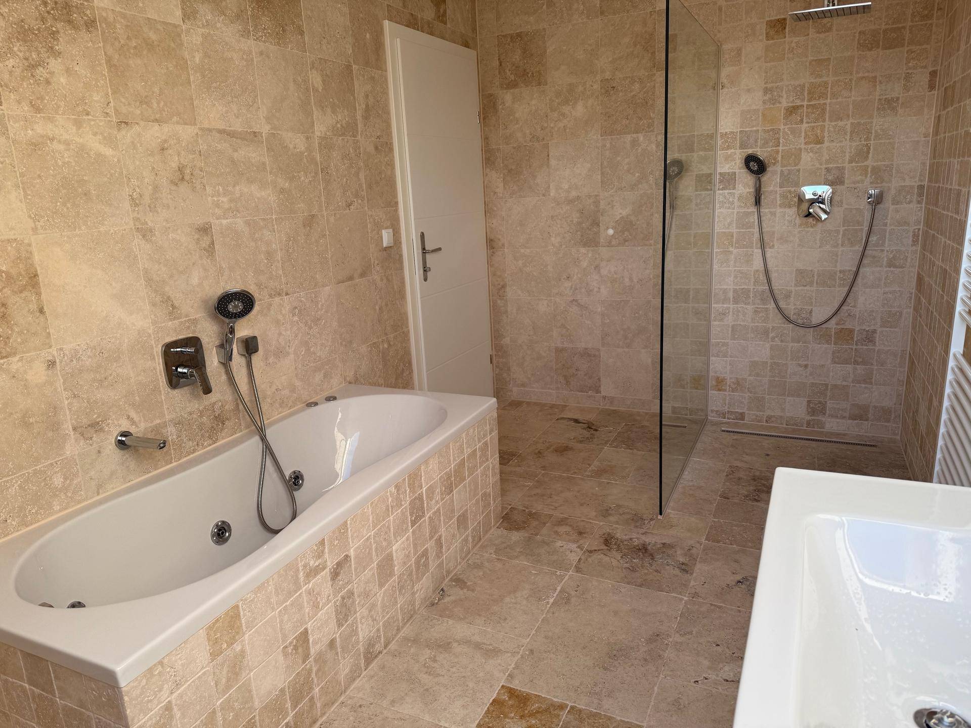 Geräumiges Badezimmer mit Badewanne, begehbarer Dusche und beigen Fliesen.