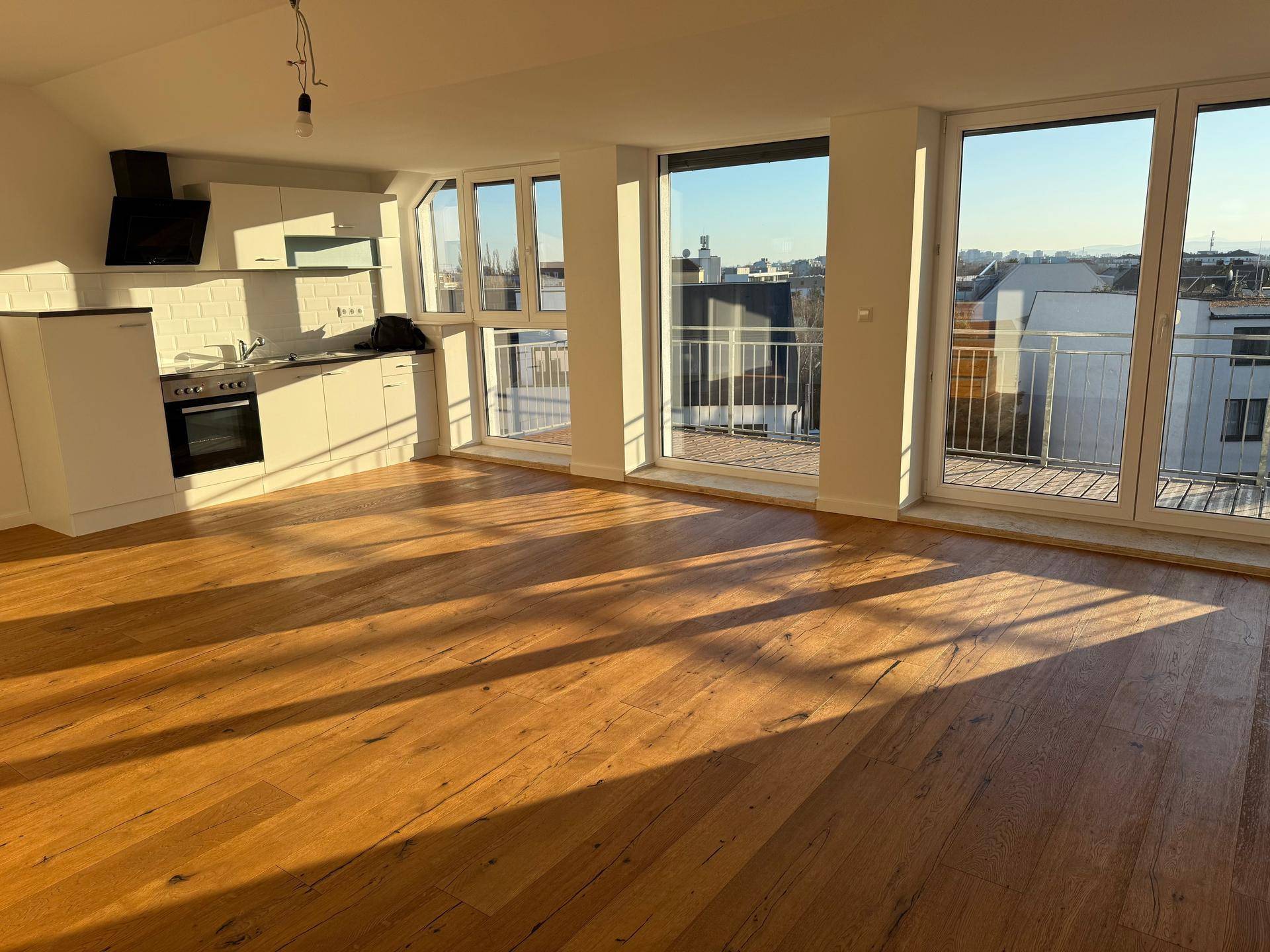 Lichtdurchfluteter Wohnbereich mit Holzboden, moderner Küche und direktem Zugang zum Balkon.