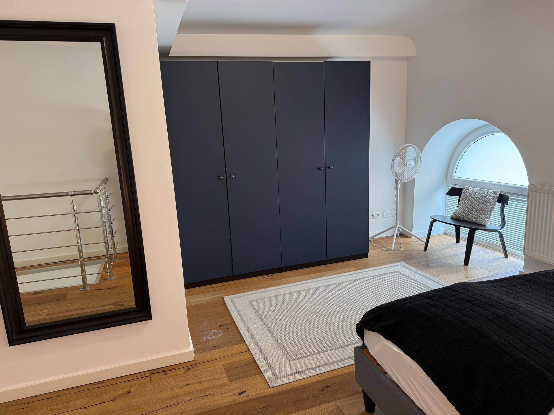 Schlafzimmer mit großen, dunkelblauen Einbauschränken, Spiegel und einem Rundbogenfenster.