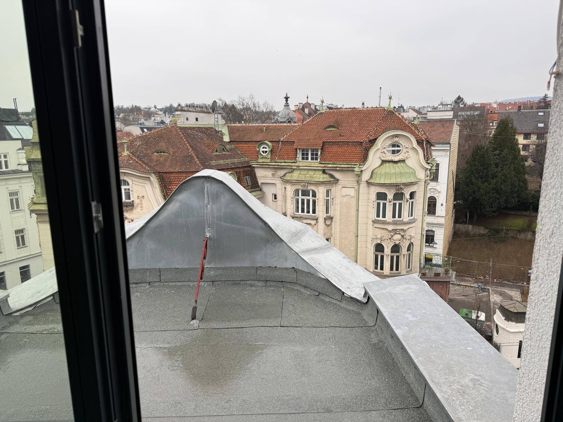 Blick aus dem Fenster auf eine Metall-Dachkonstruktion und historische Gebäude mit roten Ziegeldächern.