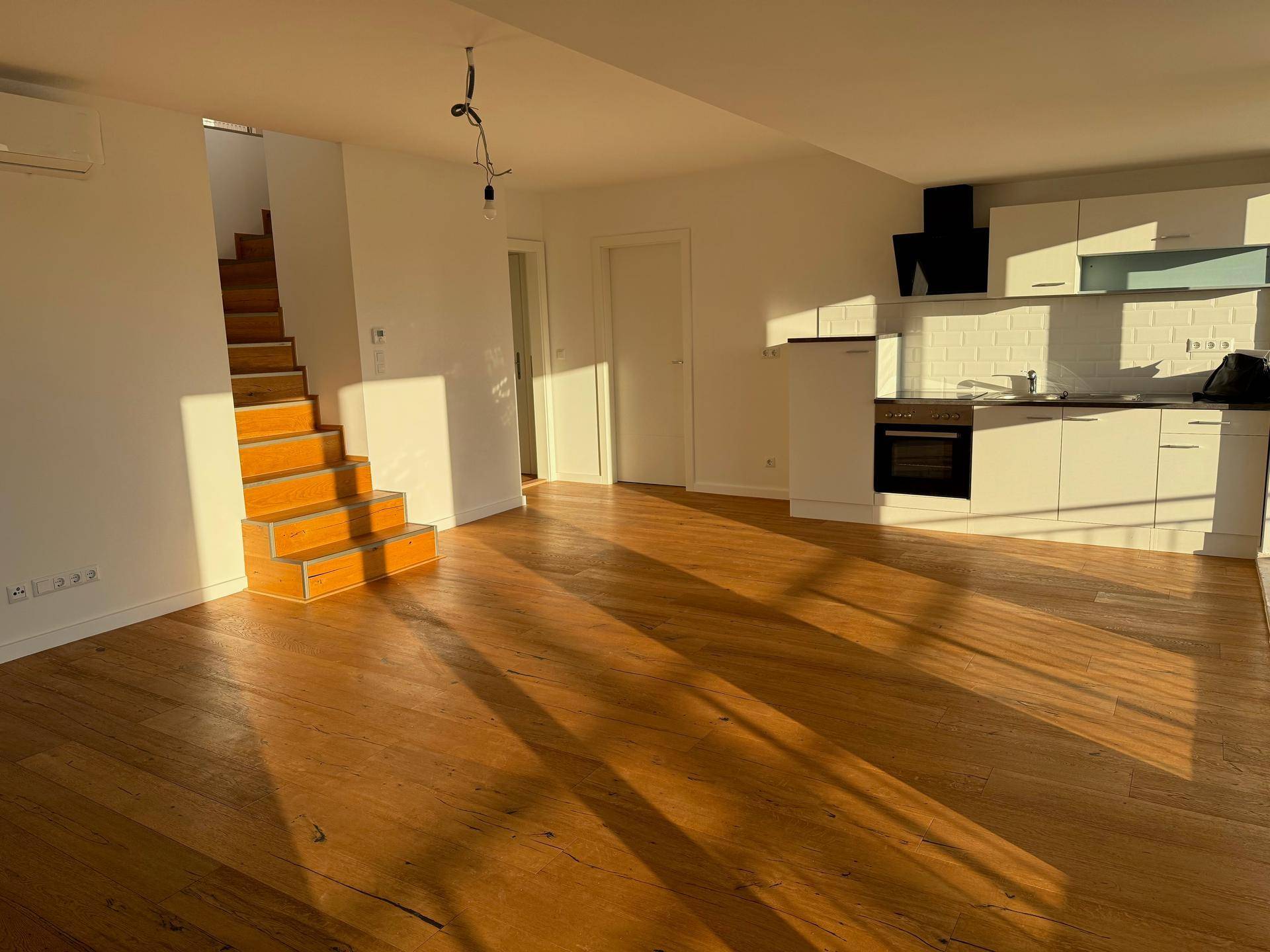Geräumiger Wohnbereich mit Holzboden, integrierter Küche und viel natürlichem Licht.