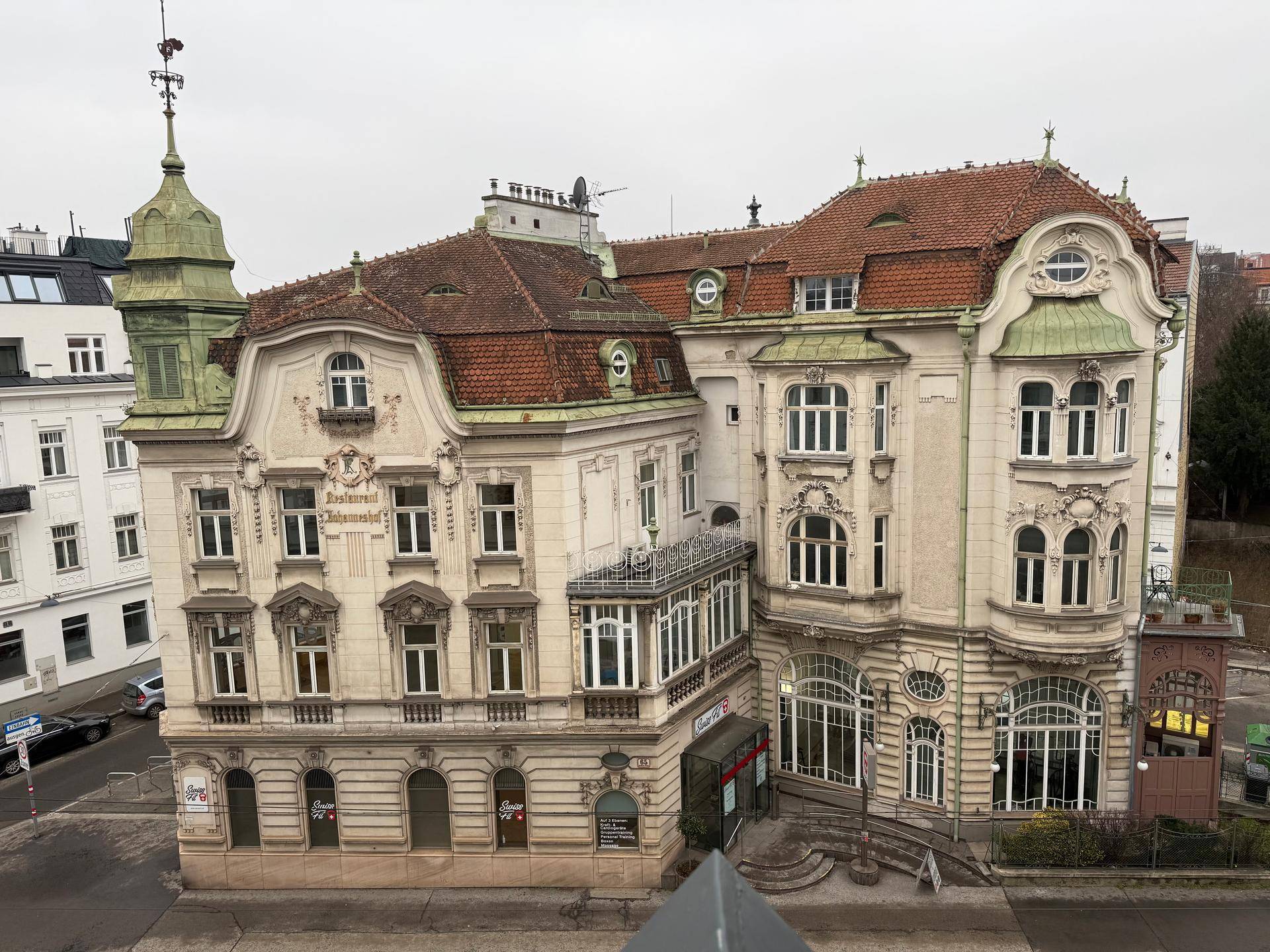 Prächtiges historisches Gebäude mit roten Ziegeldächern, grünen Kuppeln und kunstvollen Fassadendetails.