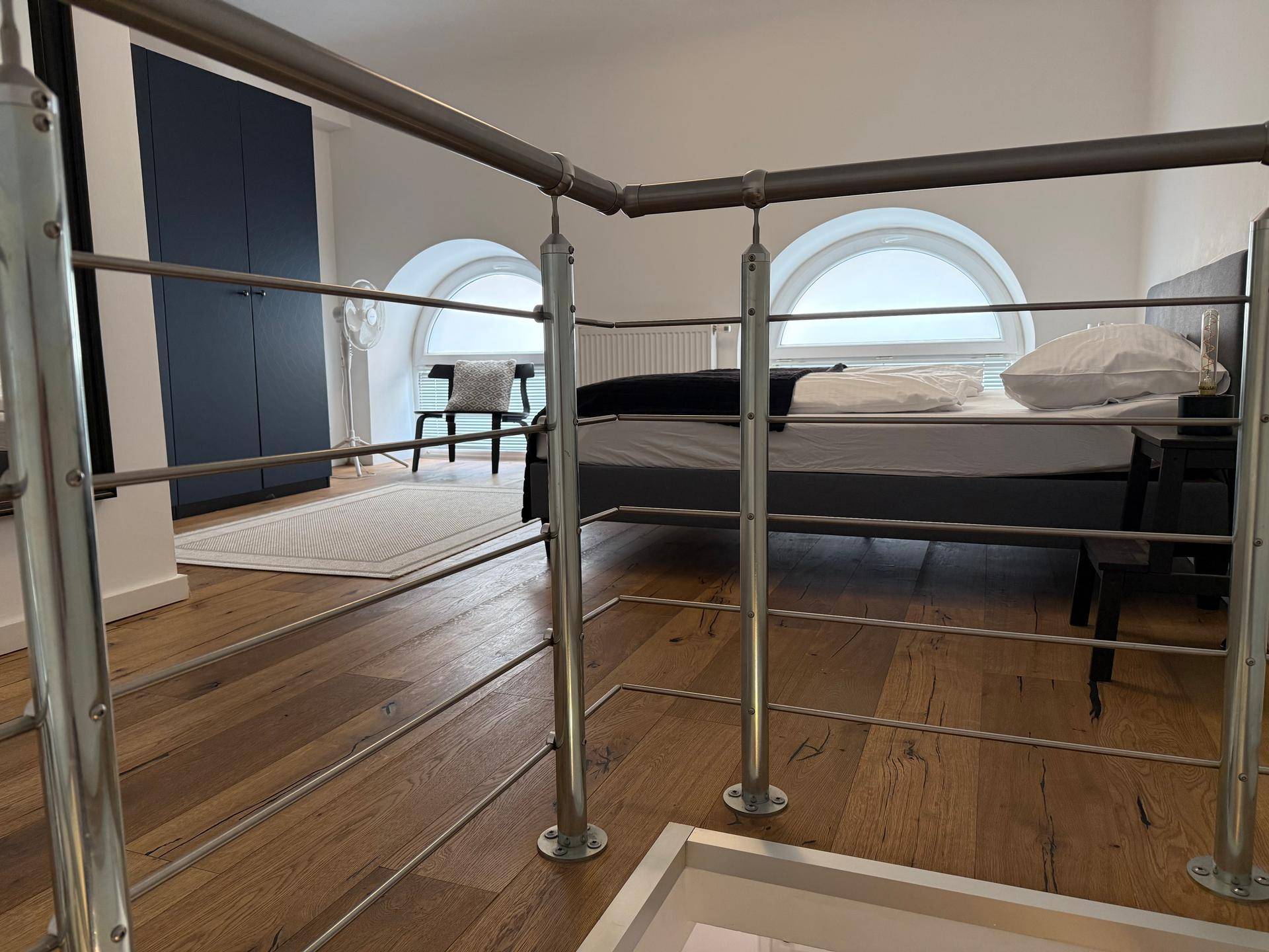 Schlafzimmer im Obergeschoss mit Holzboden, runden Fenstern und Blick auf das Bett.