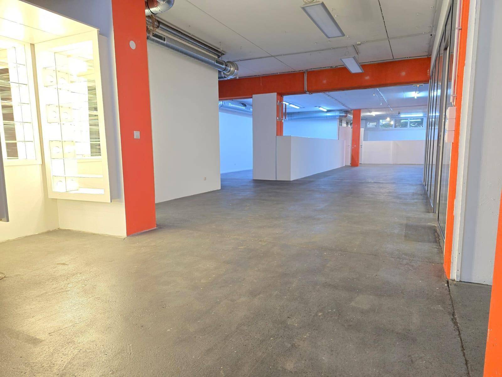 Weitläufiger, offener Gewerberaum mit orangefarbenen Säulen und sichtbaren Lüftungsrohren an der Decke.