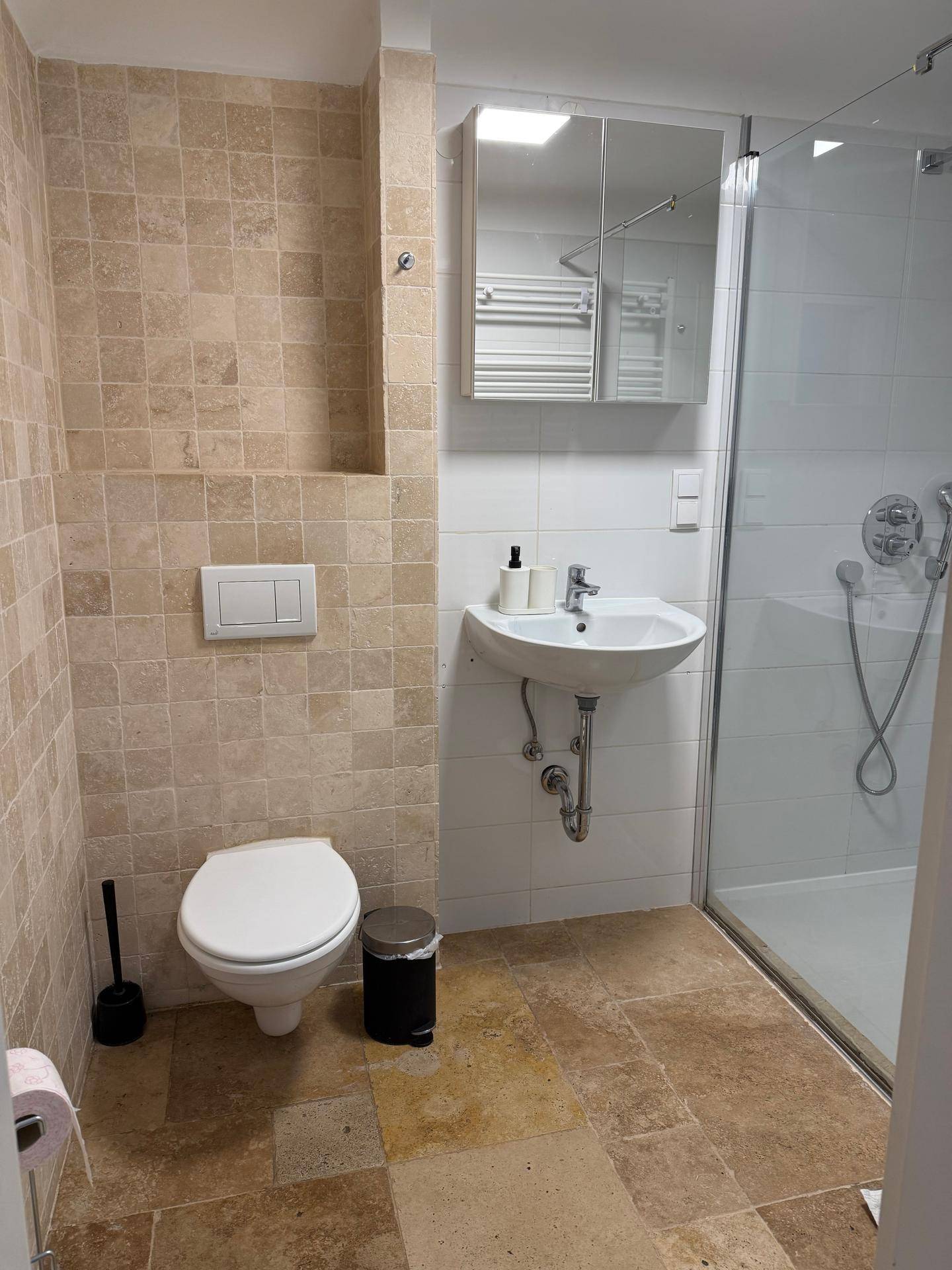 Modernes Badezimmer mit beigefarbenen Fliesen, wandhängendem WC und begehbarer Dusche.