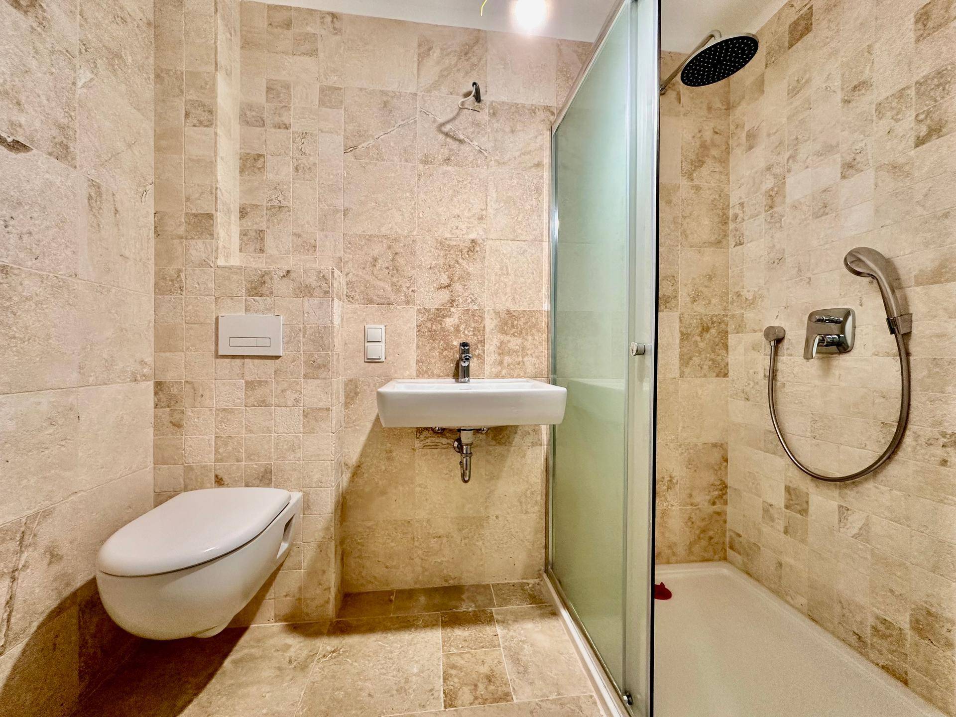 Modernes Badezimmer mit beigefarbenen Fliesen, wandhängendem WC und Duschkabine.