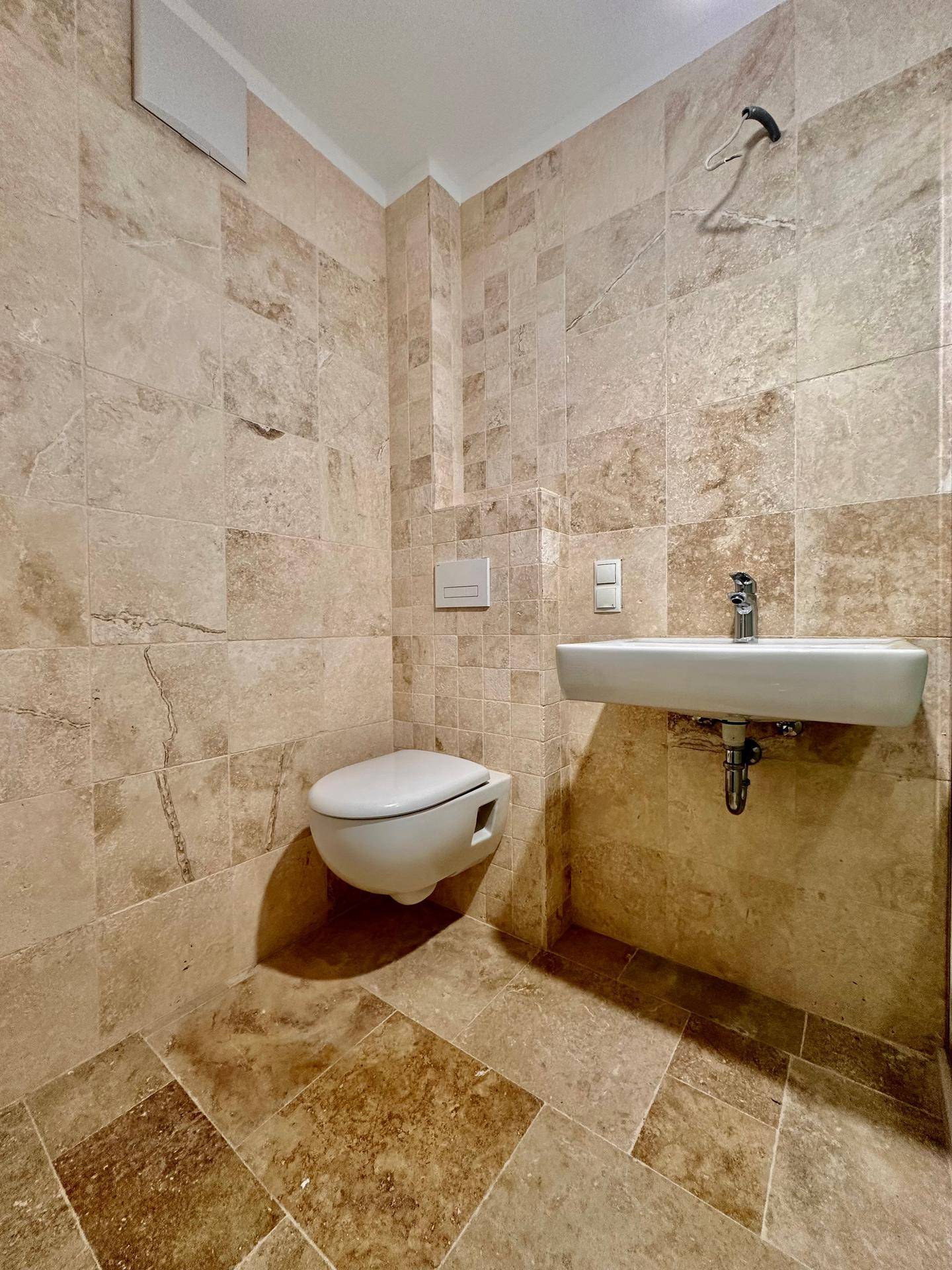 Kleines Gäste-WC mit beigefarbenen Fliesen, wandhängendem WC und modernem Waschbecken.