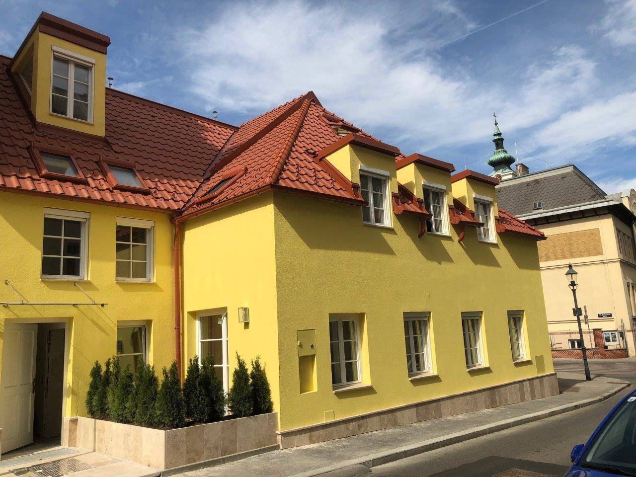 Attraktives gelbes Gebäude mit rotem Ziegeldach und mehreren Fenstern an einer ruhigen Straße.