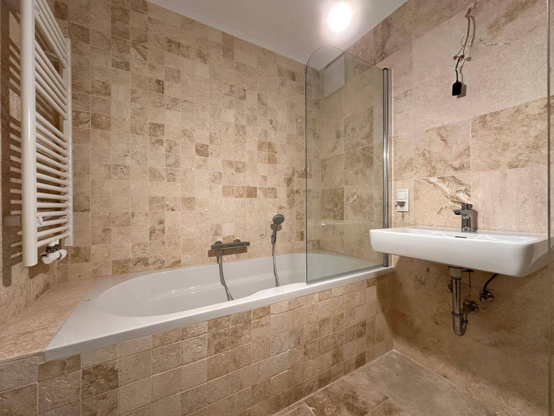 Modernes Badezimmer mit beigefarbenen Fliesen, Badewanne, Waschbecken und beheiztem Handtuchhalter.