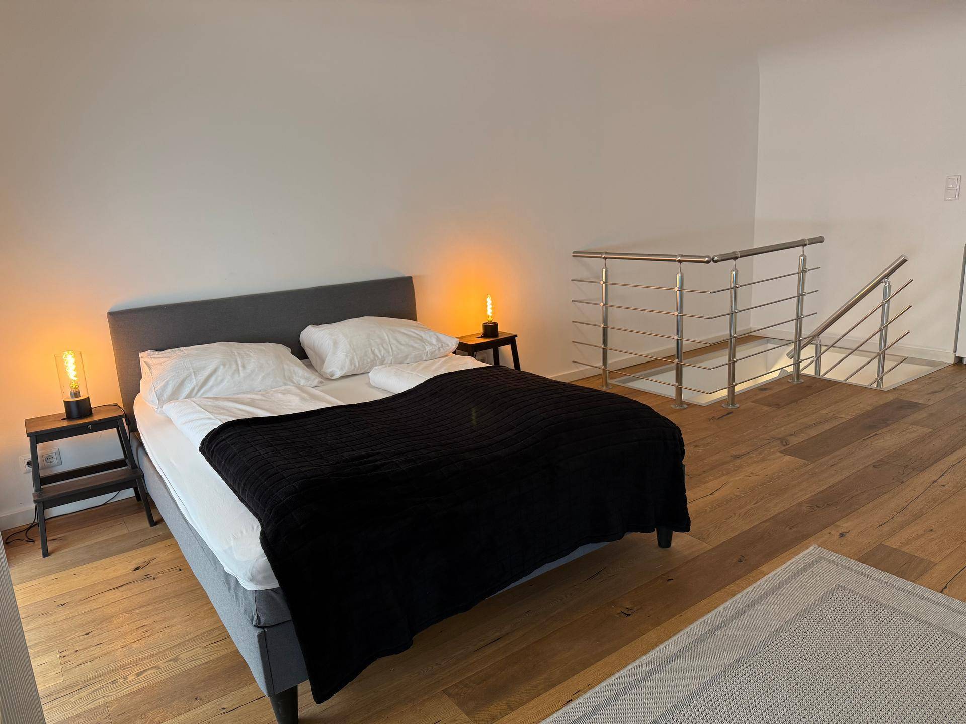 Helles Schlafzimmer mit Doppelbett, Holzboden und offener Galerie zum unteren Bereich.
