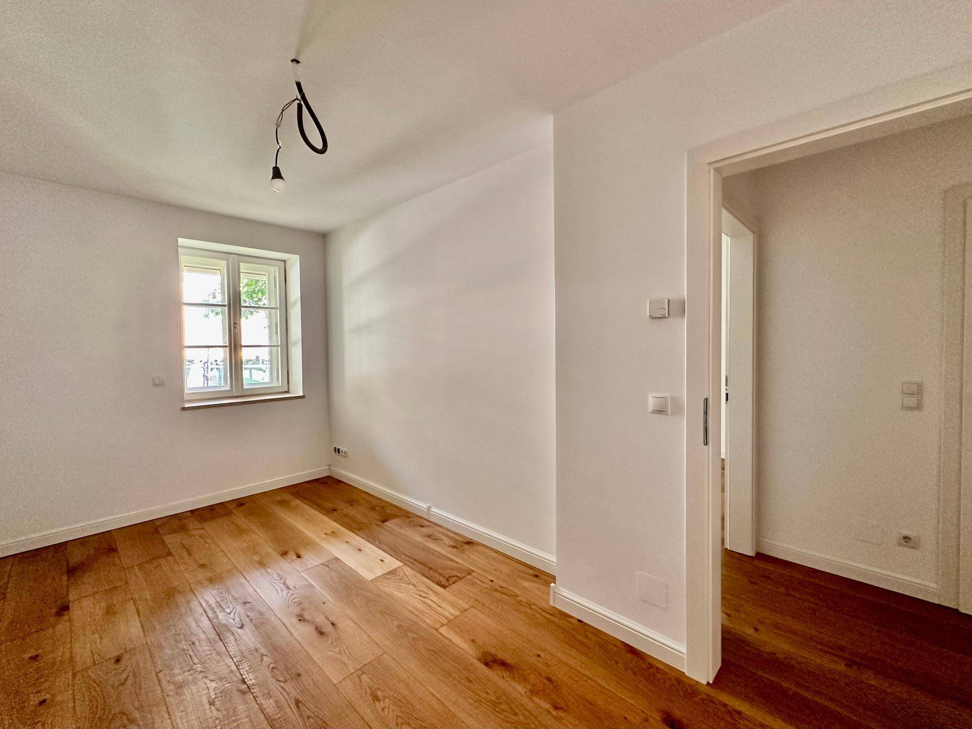 Helles Zimmer mit Holzboden und Fenster, ideal als Schlaf- oder Arbeitszimmer nutzbar.