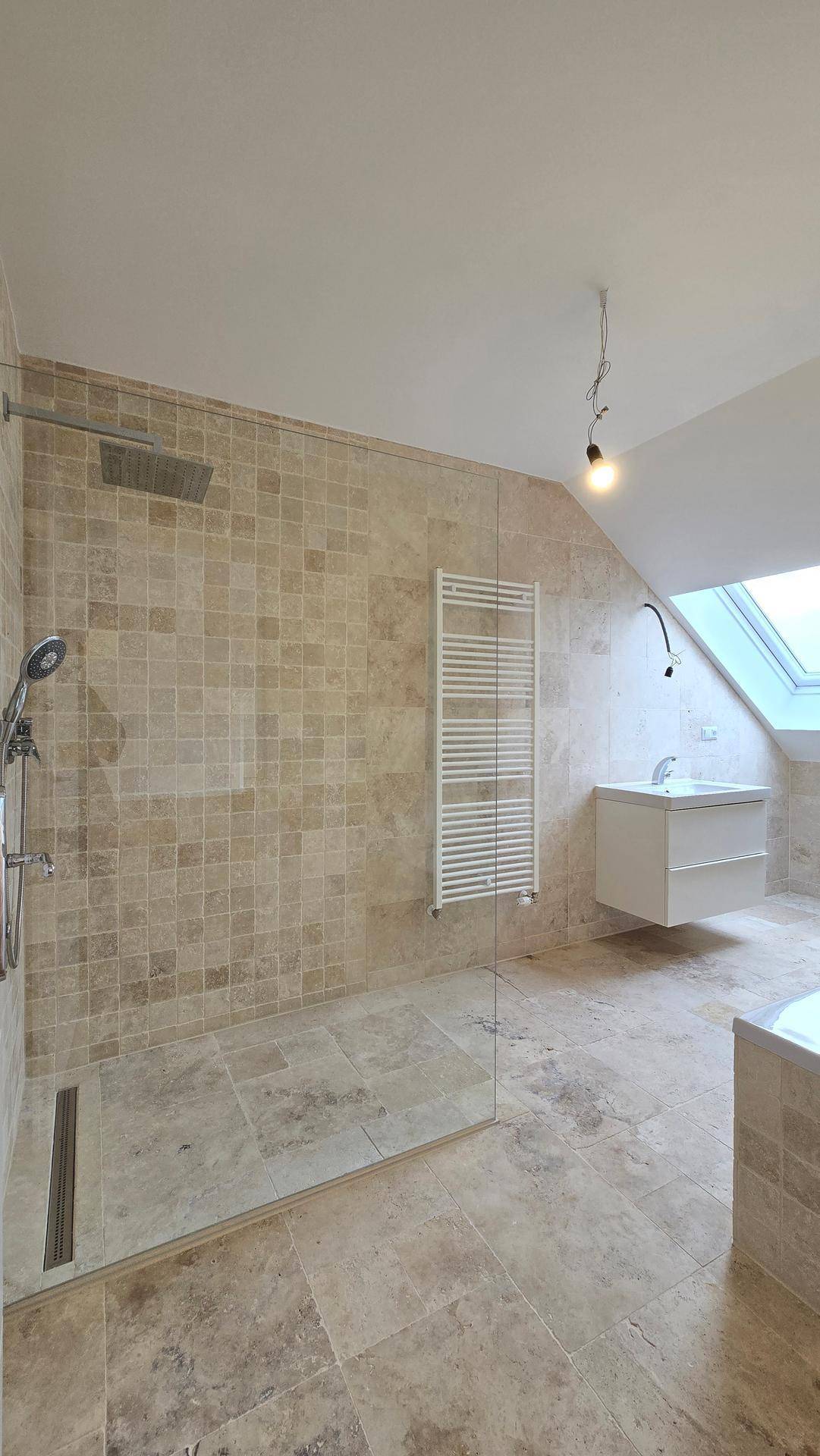 Modernes Badezimmer mit begehbarer Dusche, beigen Fliesen und Dachfenster für Tageslicht.
