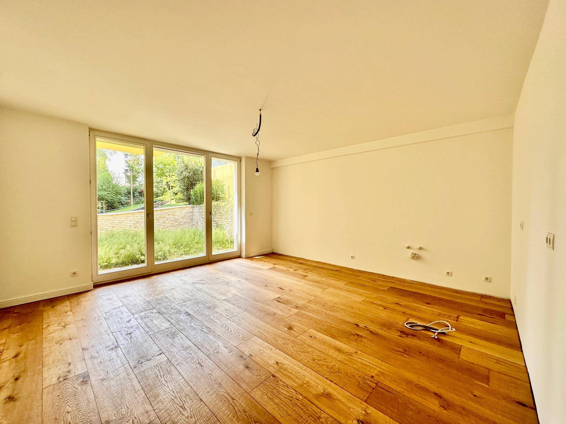 Geräumiger, heller Raum mit großen Fenstern und Holzboden, ideal als Wohnzimmer.