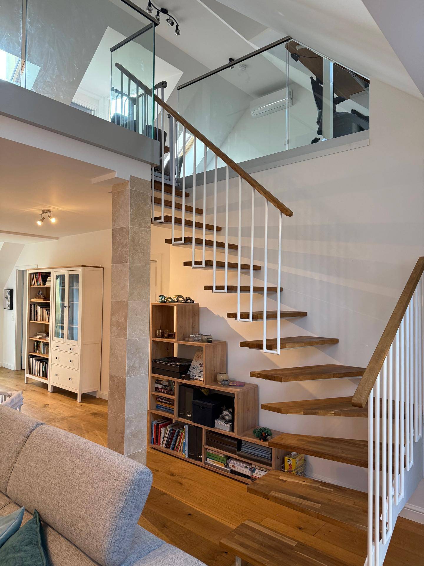 Elegante Holztreppe mit Glasgeländer und integrierten Bücherregalen im Wohnbereich.