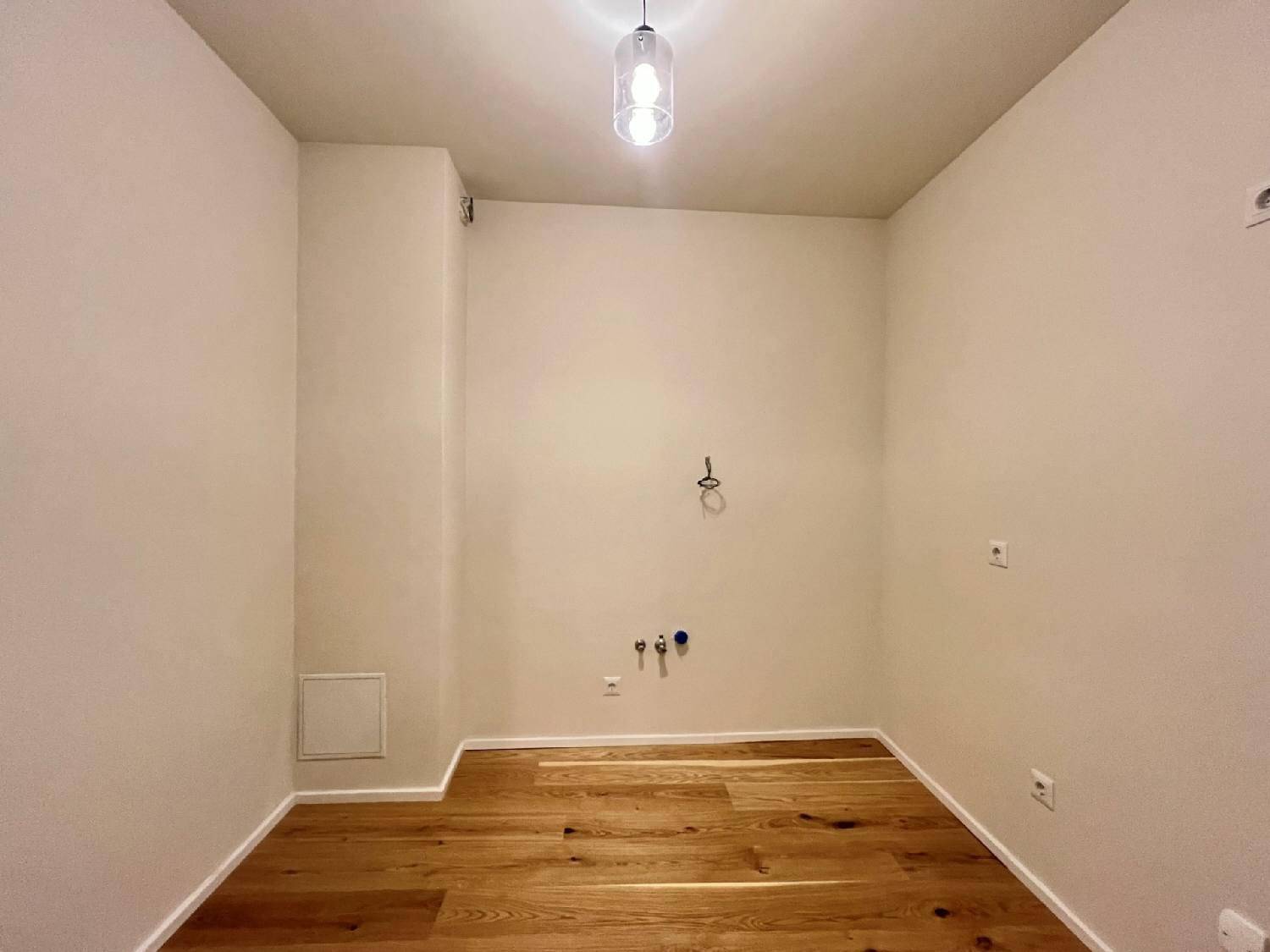 Raum mit Holzparkettboden und Anschlüssen für eine mögliche Küchenzeile oder Waschküche.