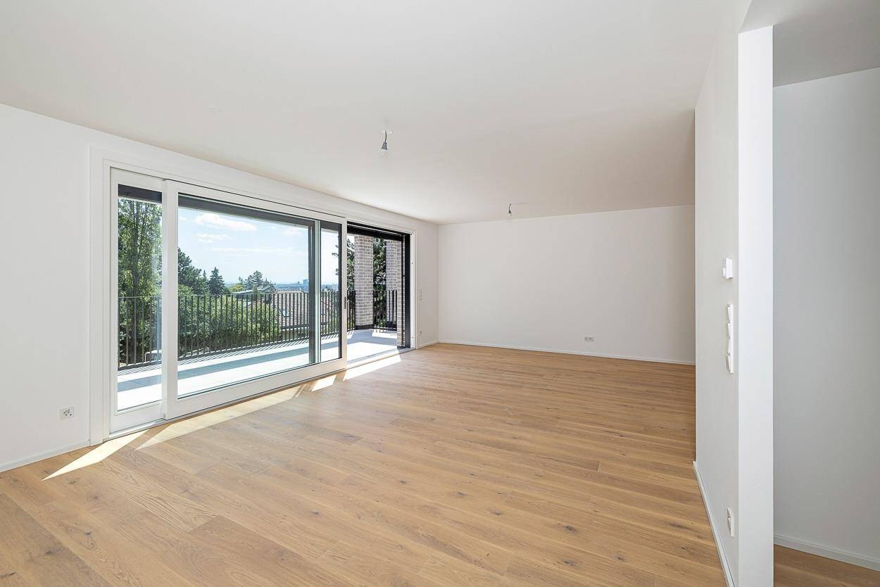 Lichtdurchfluteter Wohnbereich mit hellem Parkettboden und Zugang zu einem großen Balkon.
