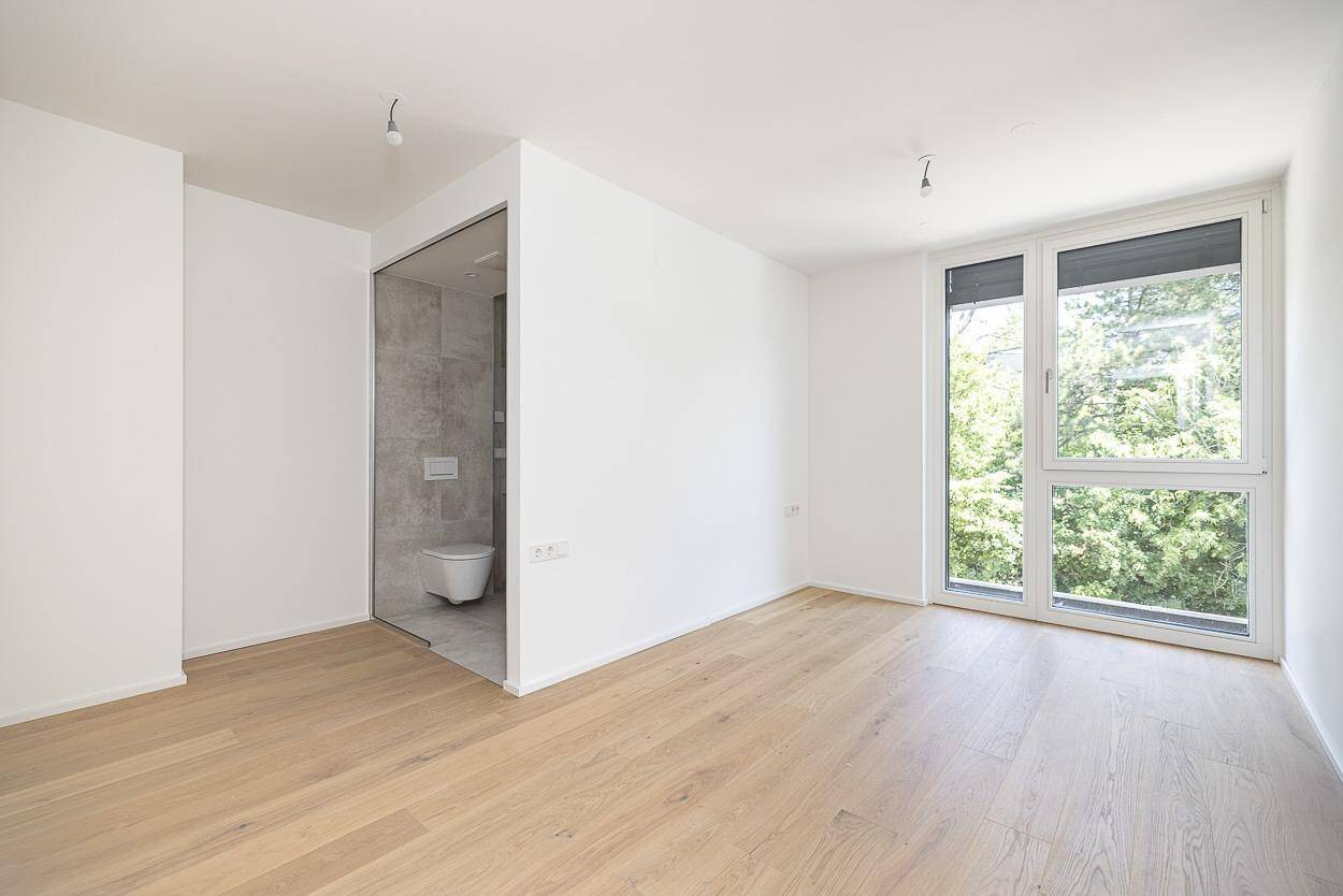 Schlafzimmer mit Holzboden und direktem Zugang zu einem modernen Badezimmer.