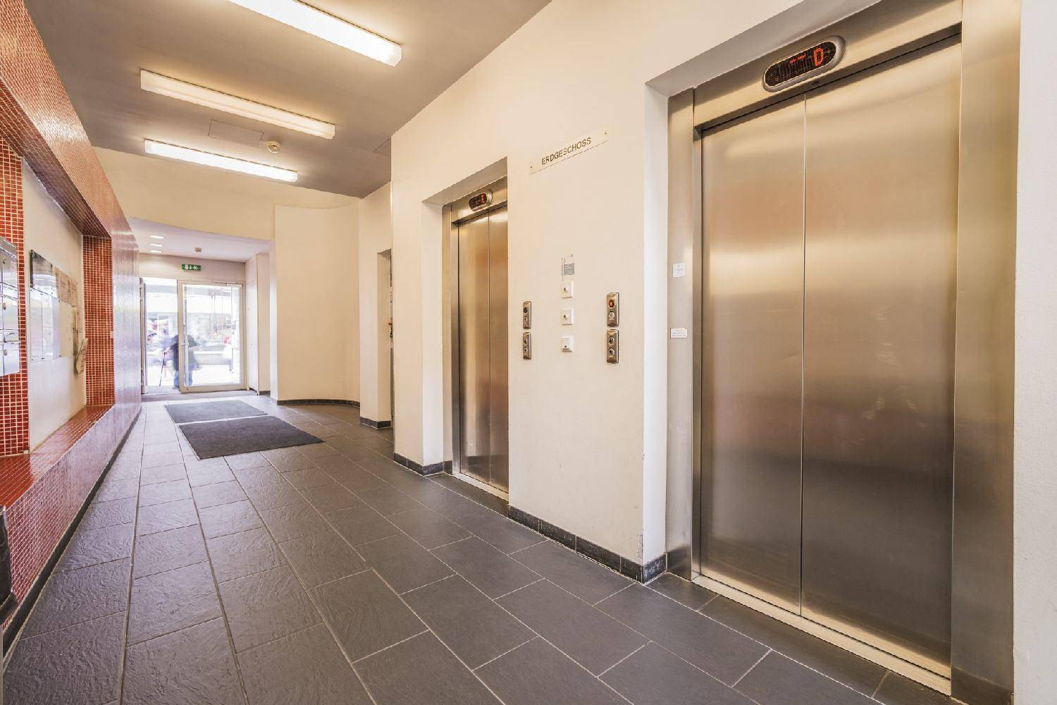 Moderner Eingangsbereich mit zwei Aufzügen, Fliesenboden und Zugang zum Treppenhaus.