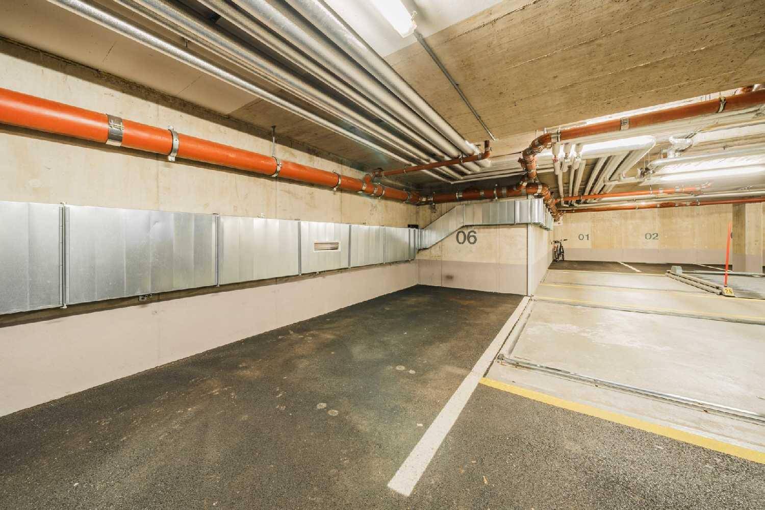 Sauberer Stellplatz in einer Tiefgarage mit sichtbaren Rohren und Lüftungsschächten an der Wand.