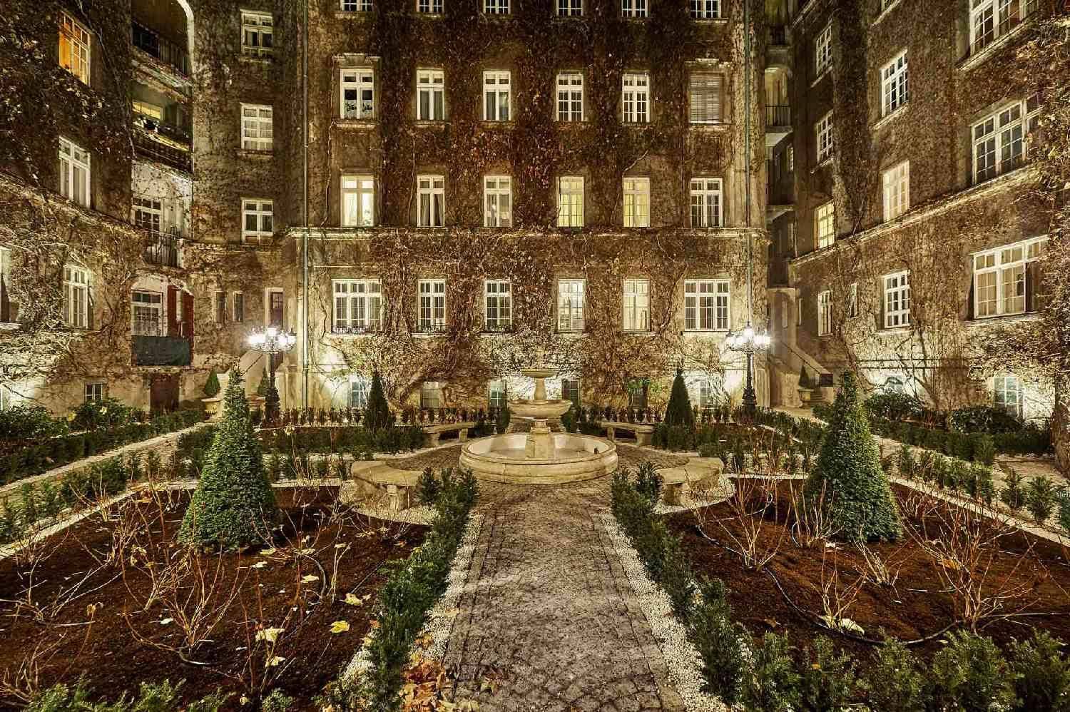 Malerischer Innenhof mit einem zentralen Brunnen, umgeben von Bäumen und Sträuchern.
