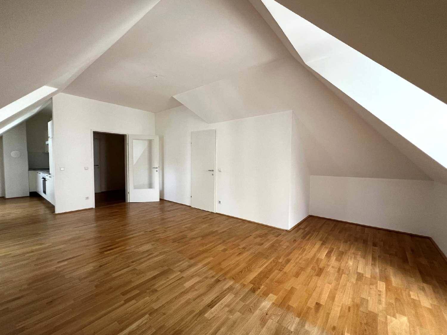 Geräumiges Zimmer im Dachgeschoss mit Holzboden, schrägen Wänden und Zugang zur Küche.