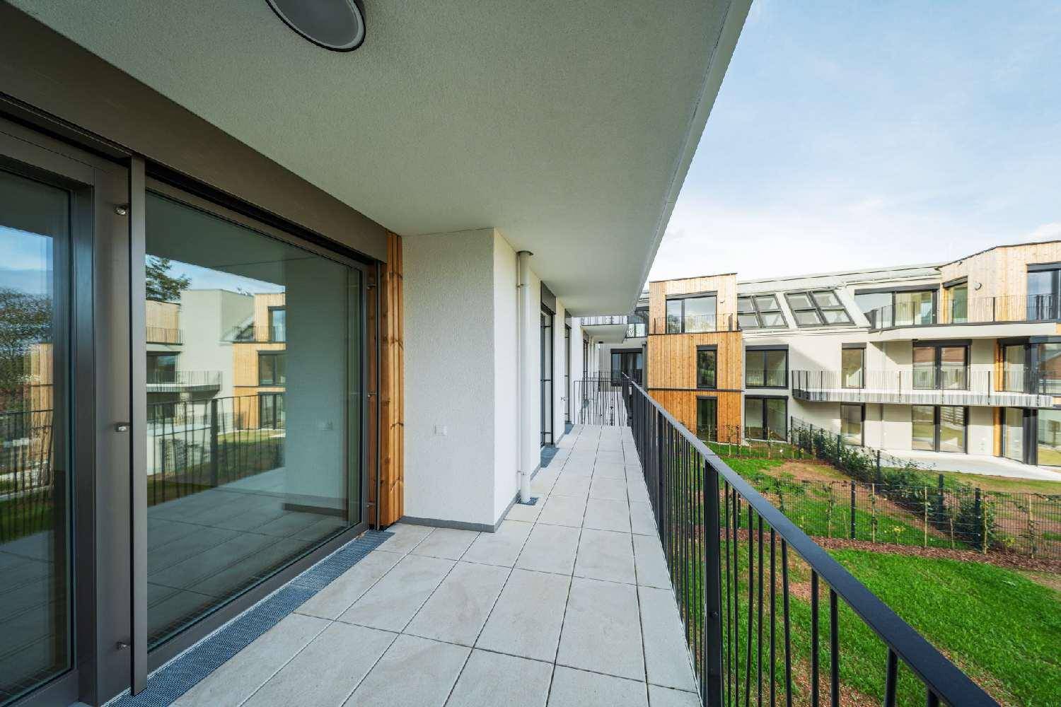 Langer Balkon mit Fliesenboden und Blick auf die moderne Wohnanlage und Grünflächen.