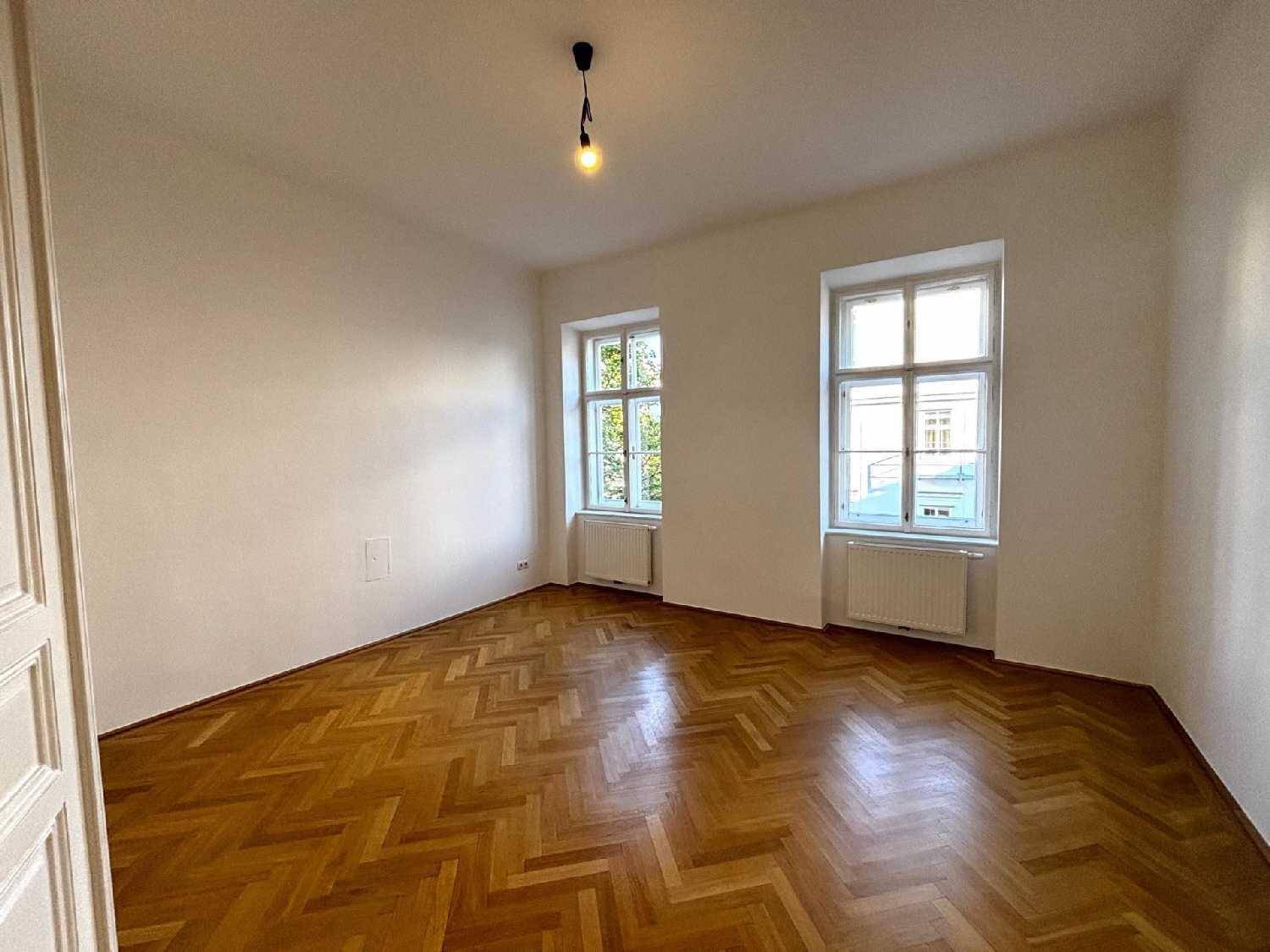 Helles Schlafzimmer mit klassischem Fischgrätparkett und zwei Fenstern für viel Tageslicht.