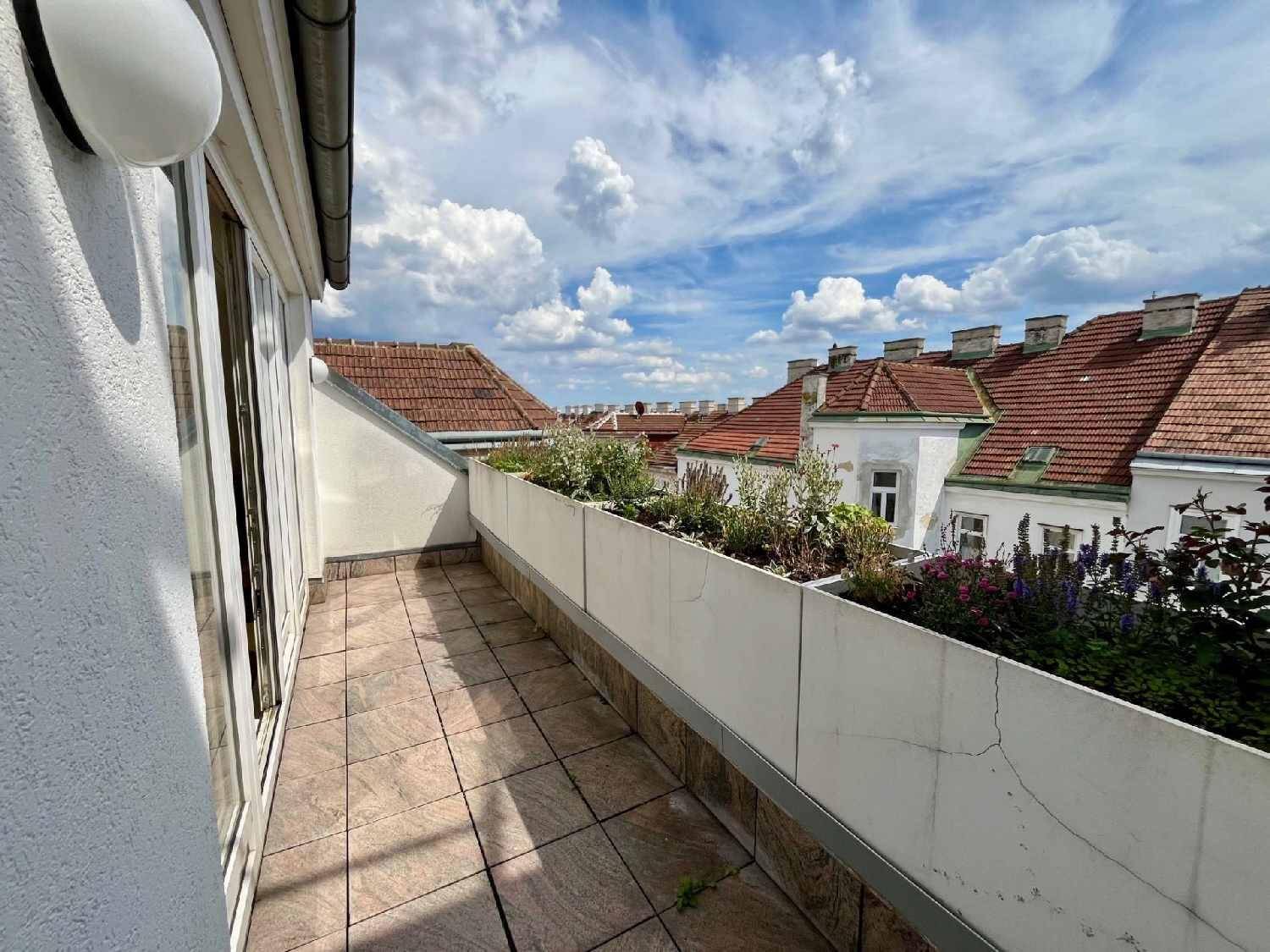 Schmaler Balkon mit Fliesenboden und Pflanzenkübeln, bietet einen Blick über die umliegenden Dächer.