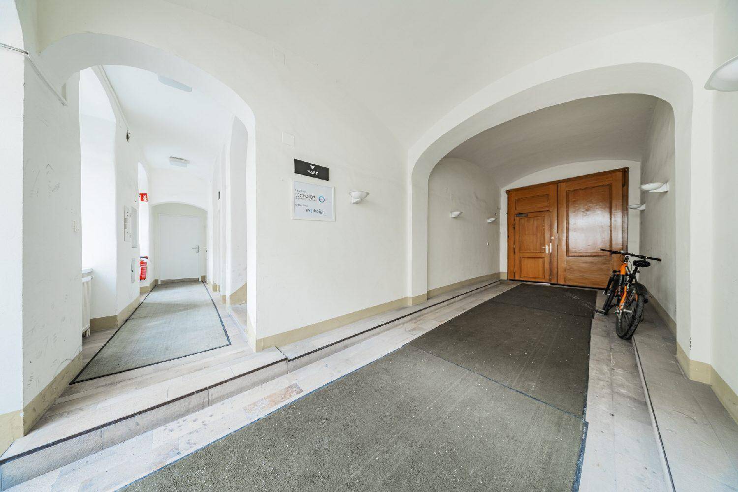 Geräumiger Eingangsbereich mit Rampe, hohen Decken und Holztüren, ideal für Fahrräder.