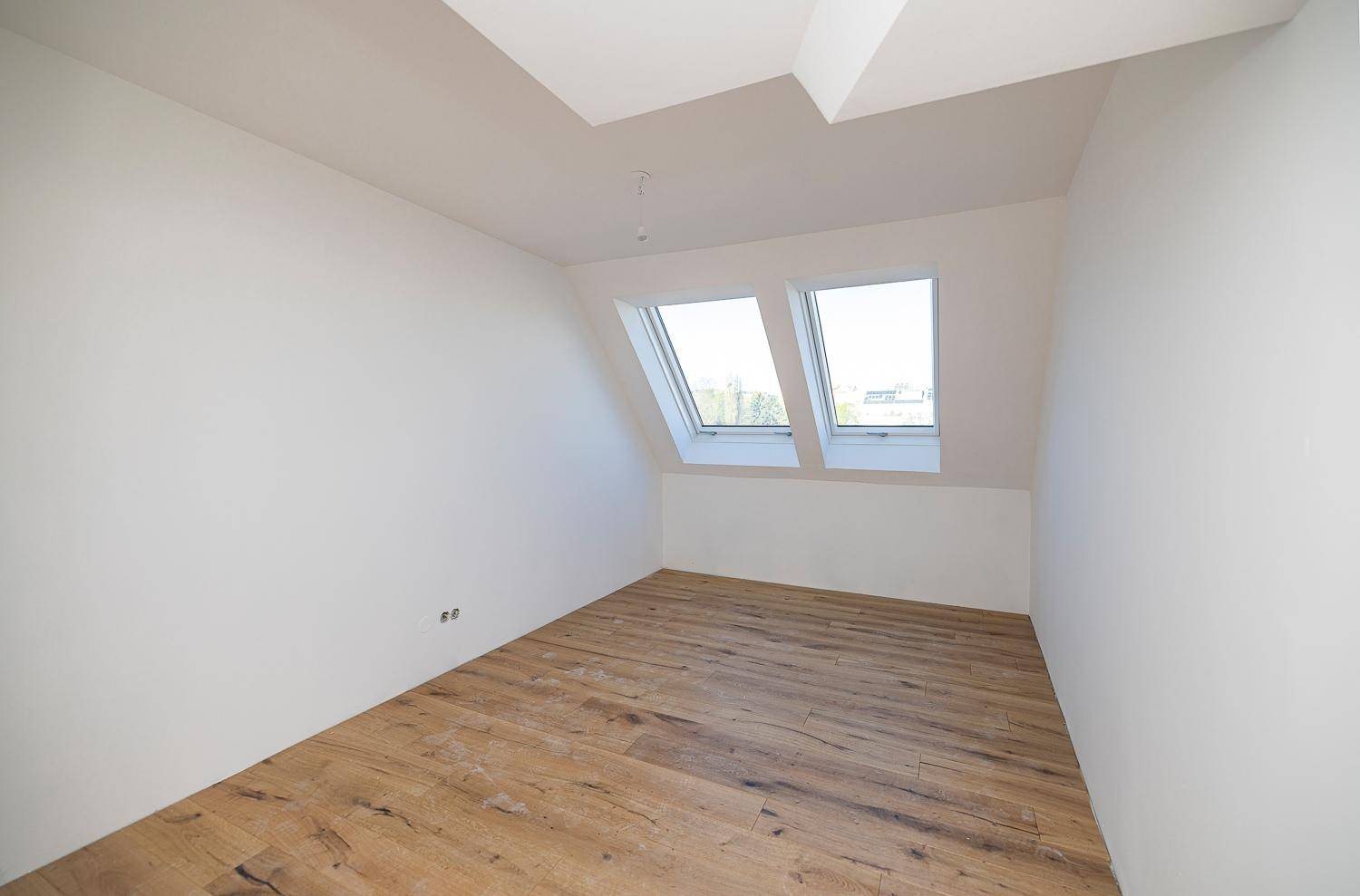 Leeres Schlafzimmer mit Holzboden und zwei Dachfenstern, ideal für viel Tageslicht.